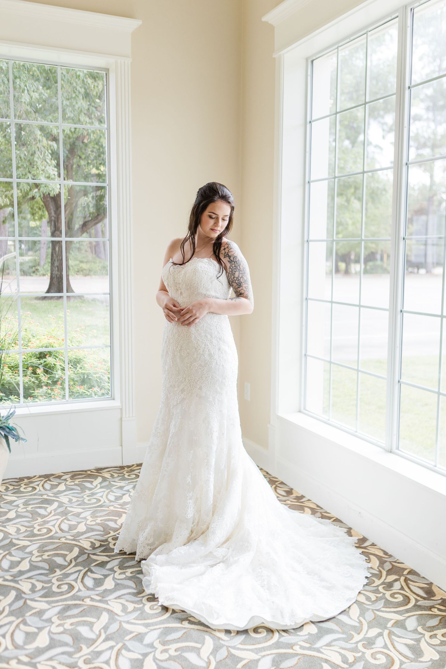 A bride in a flowing white lace gown twirls gracefully in a sunlit room with patterned tile floors and large windows.