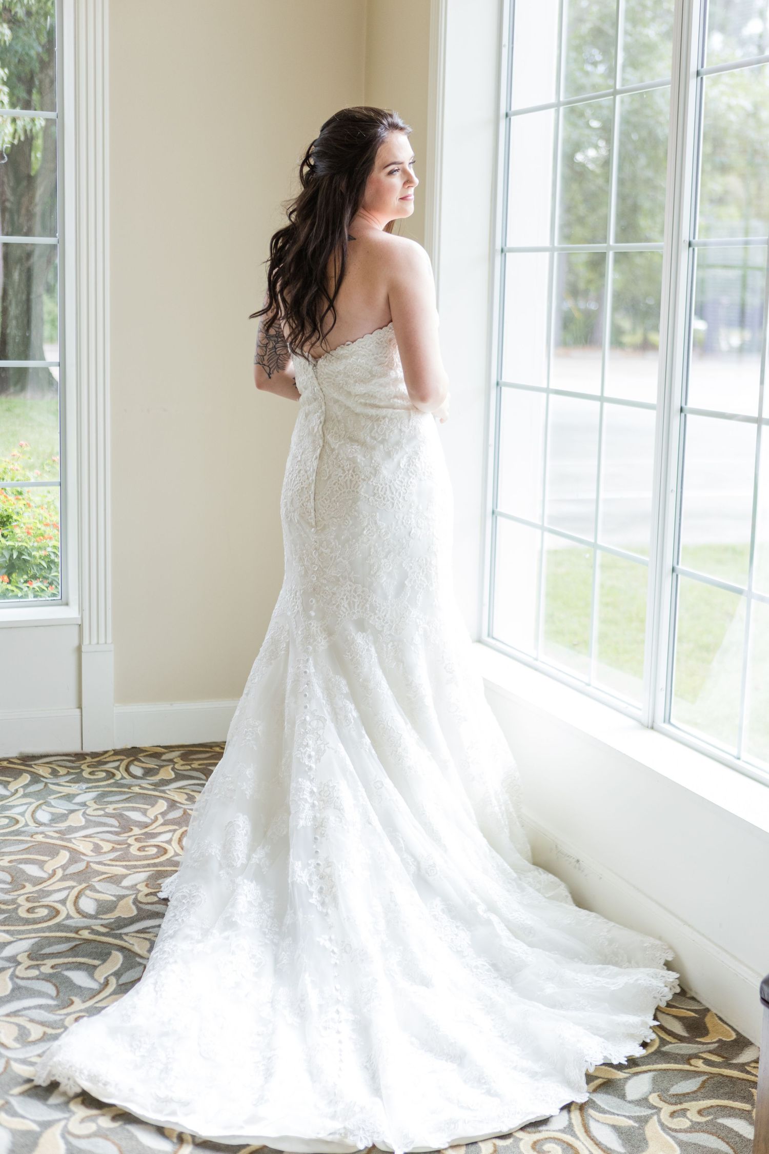 Elegant wedding dress with lace details and flowing train captured in natural window light.