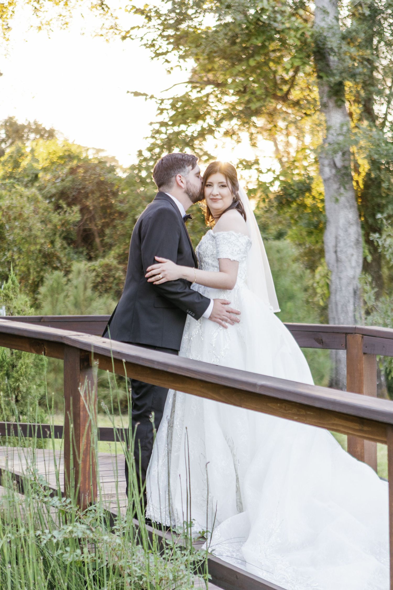 Romantic sunset portrait on wooden bridge with greenery backdrop.