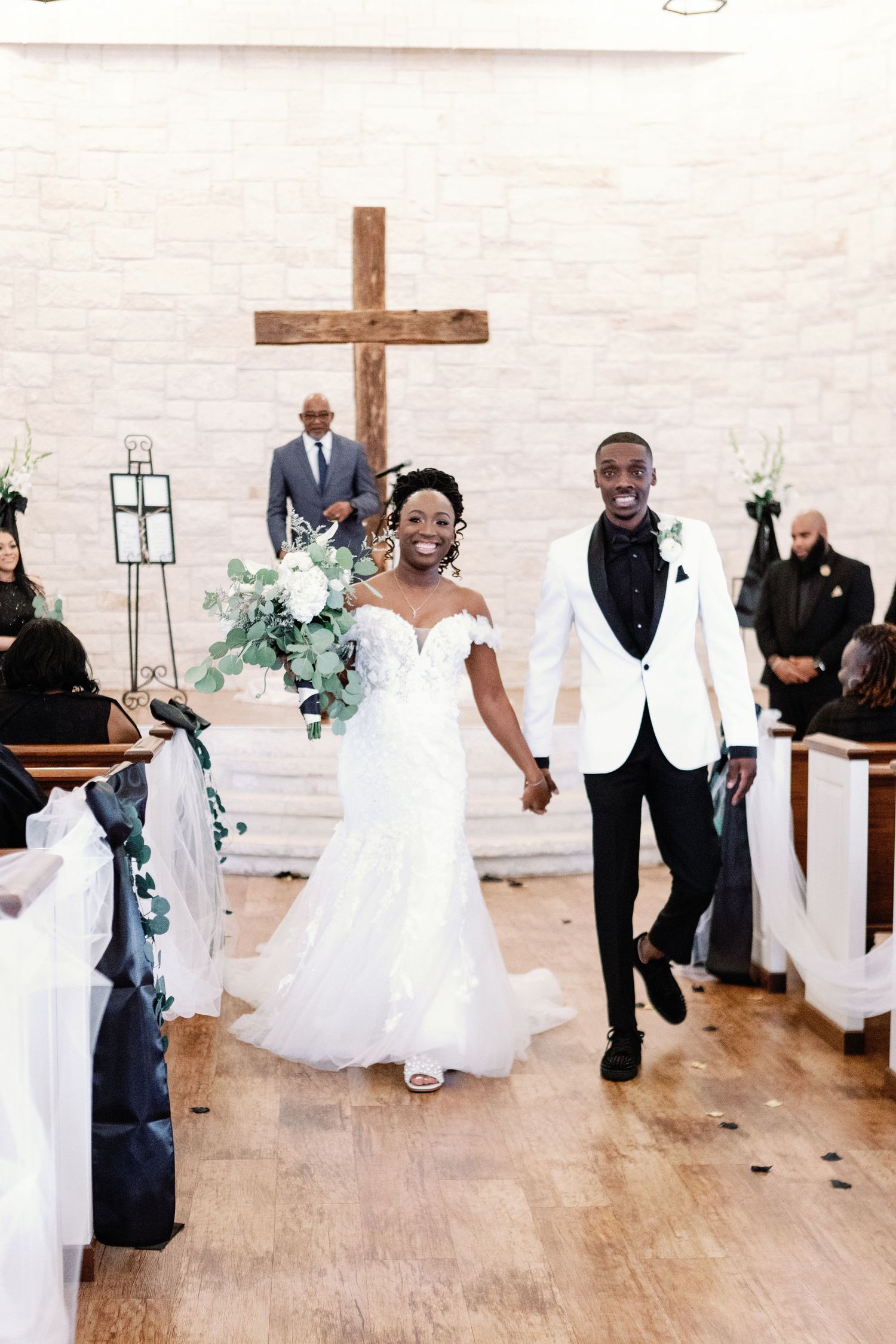 Wedding party gathered at a modern white chapel with wooden floors and cross decor.