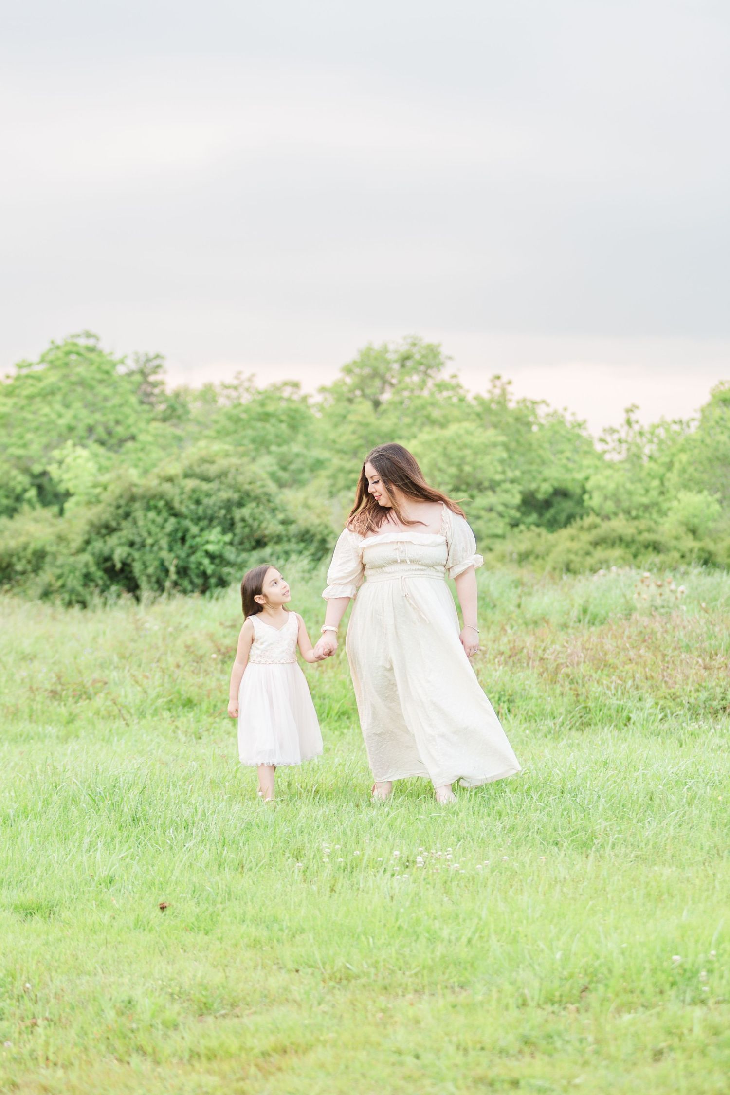 People in white dresses walking through a sunny meadow with wildflowers.