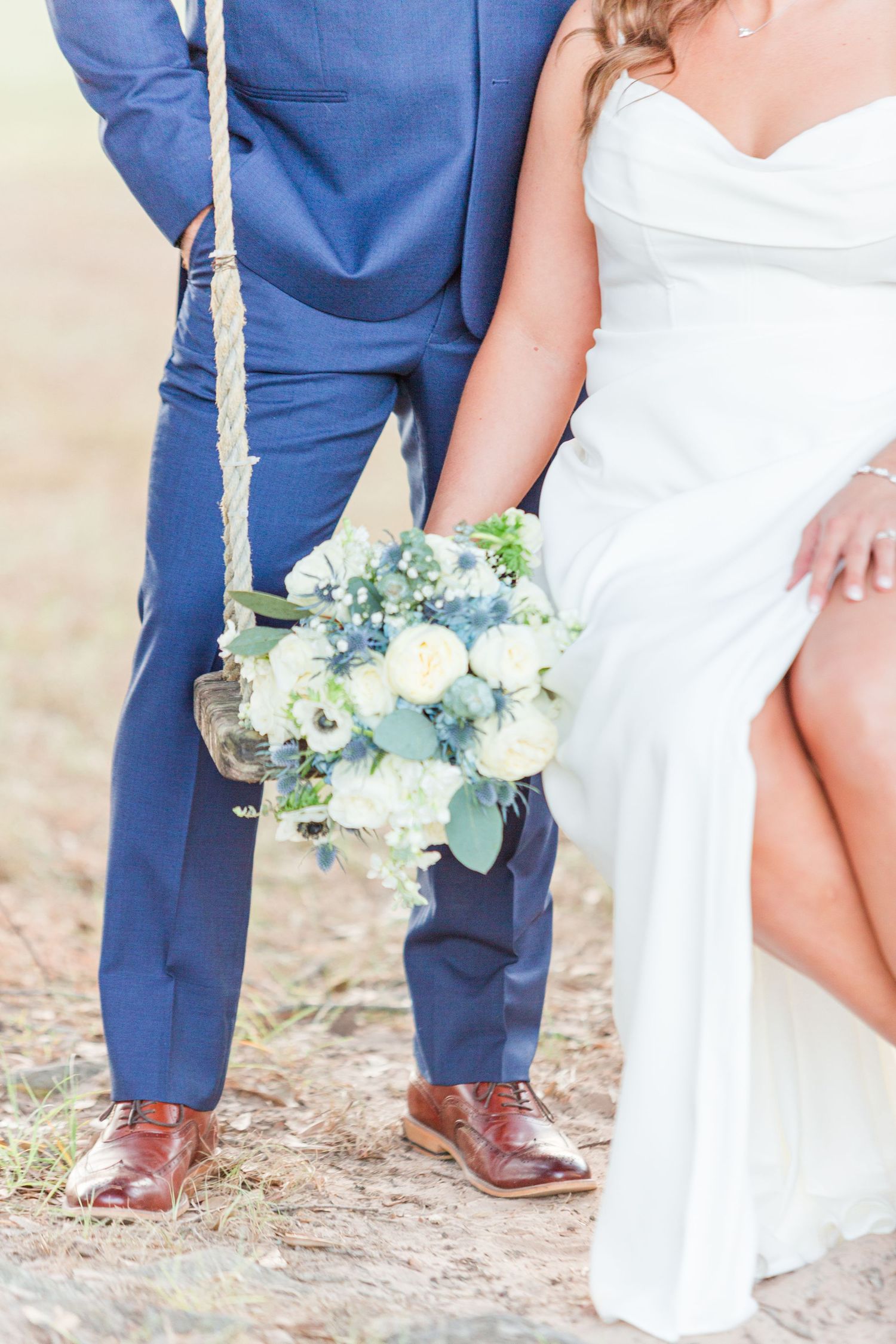 Wedding couple's lower bodies showing navy suit and white dress with delicate bouquet.