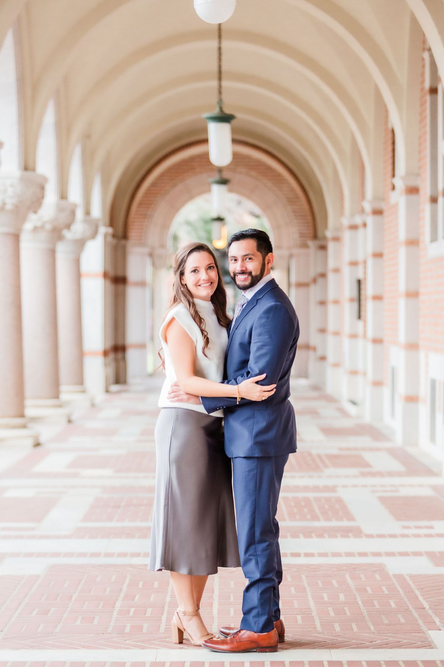 Couple stands together in beautiful colonnade hallway with arched ceilings.