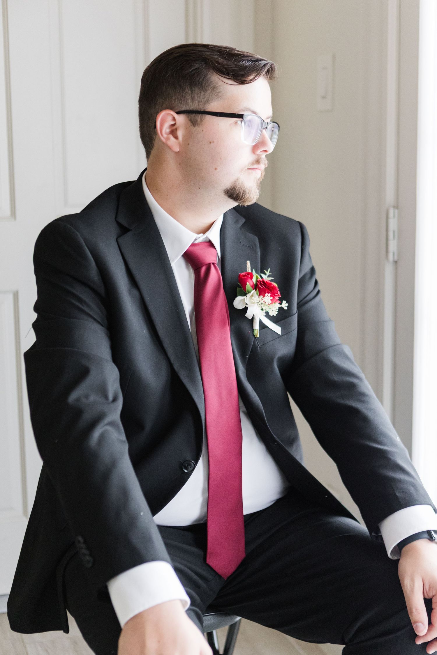 Candid shots of groom seated in formal black suit and crimson tie.