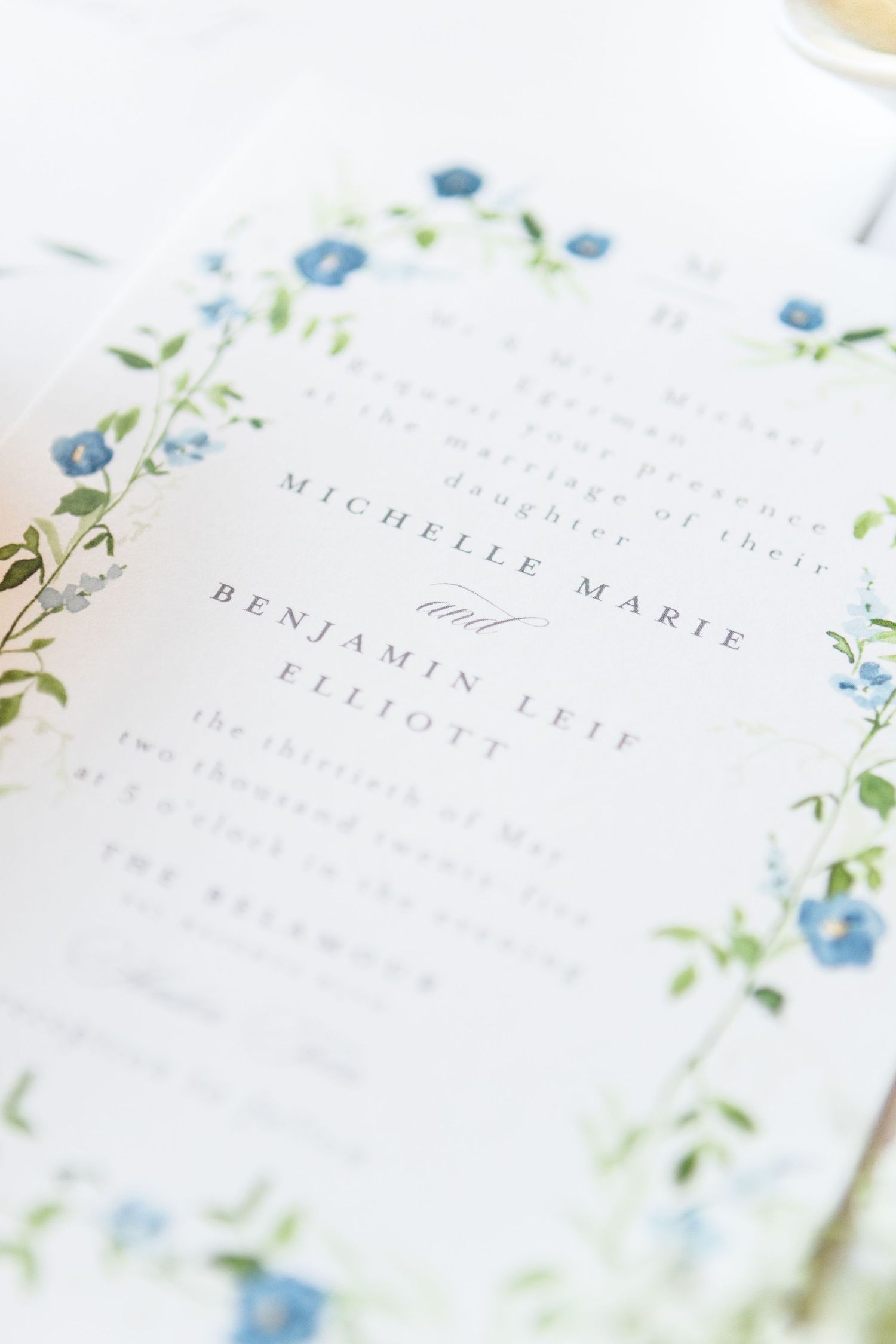Close-up of wedding invitation text with delicate blue floral border details.
