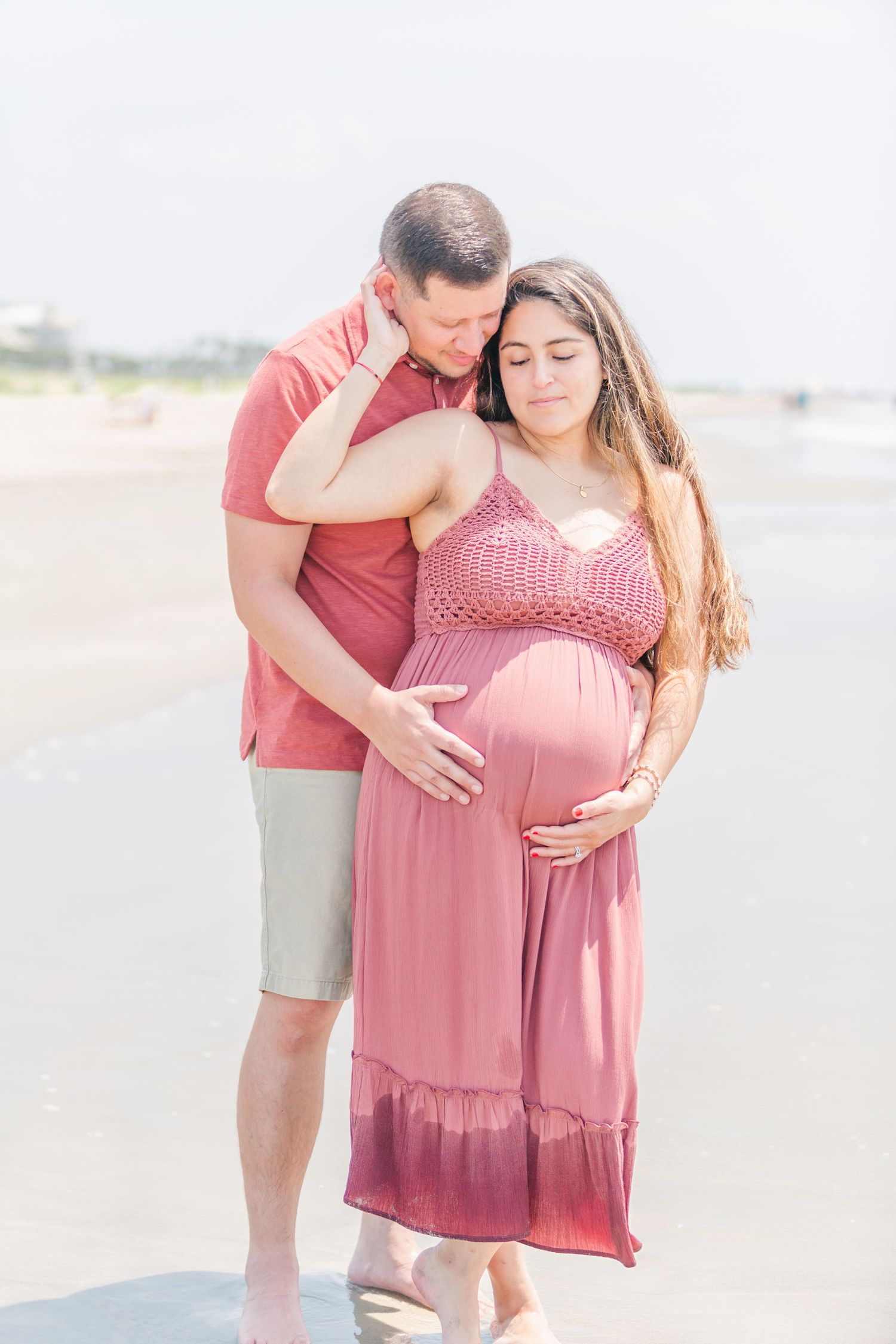 Couple embracing on a misty beach with expecting mother wearing a flowing mauve dress.