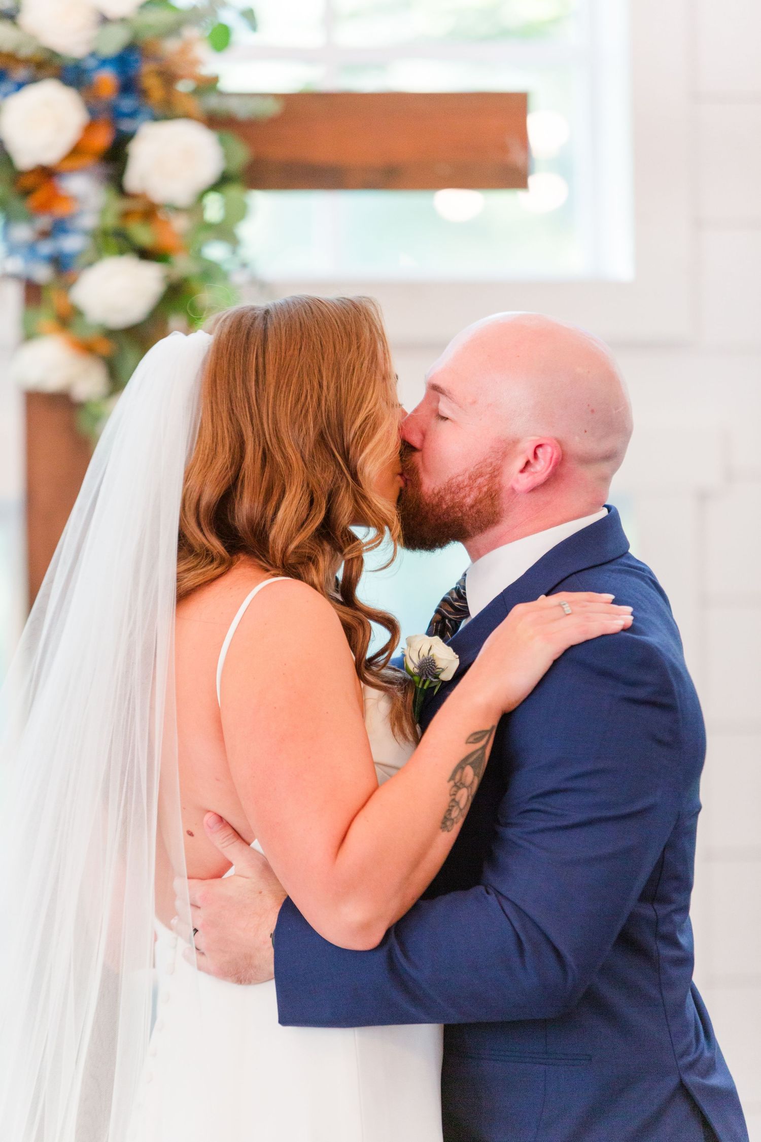 Intimate wedding moment captured in a bright indoor venue with floral decorations.
