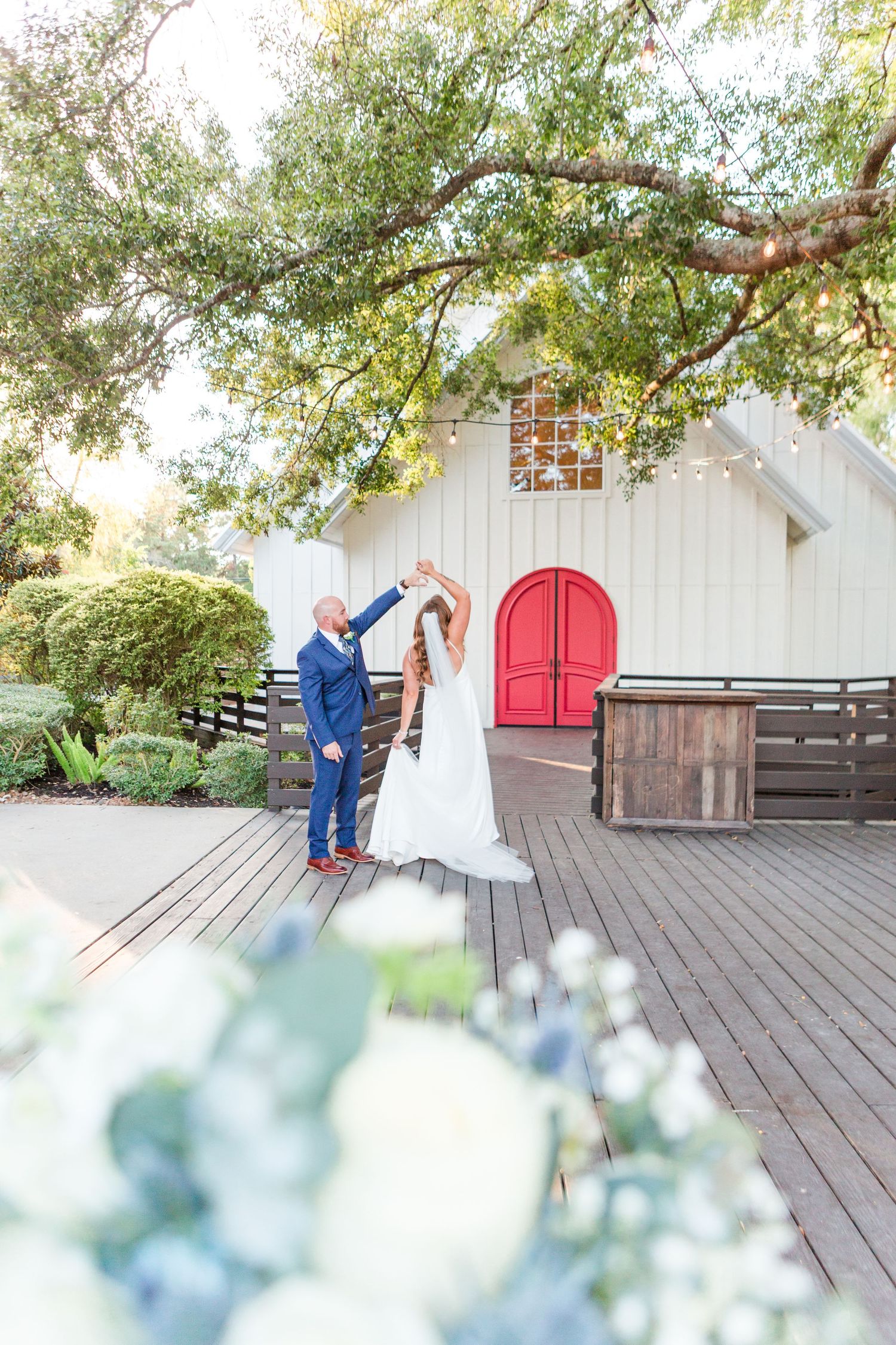 Garden wedding venue with rustic white chapel, red doors and lush green trees.