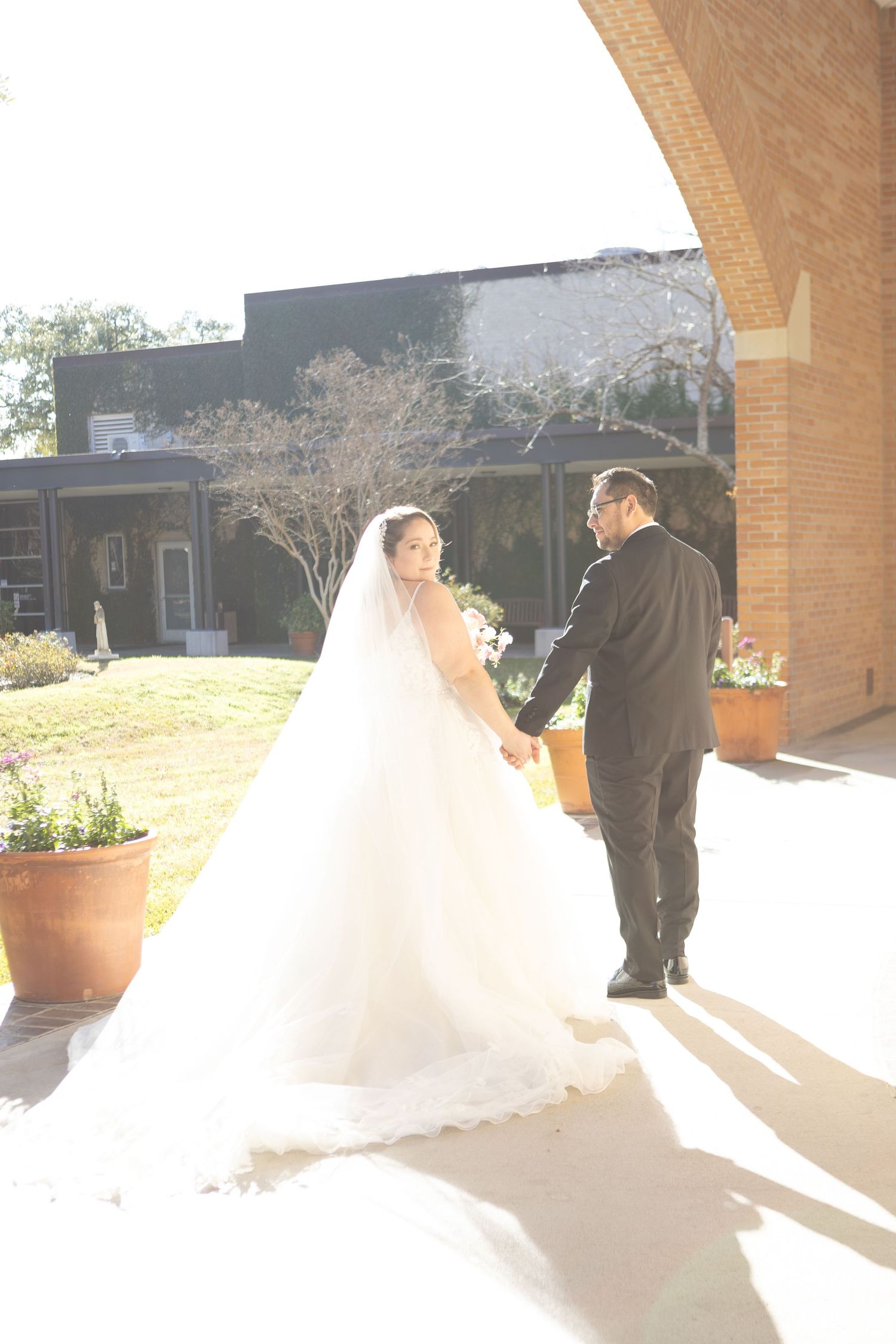 Wedding couple under brick archway with sunlight streaming through creating romantic shadows.
