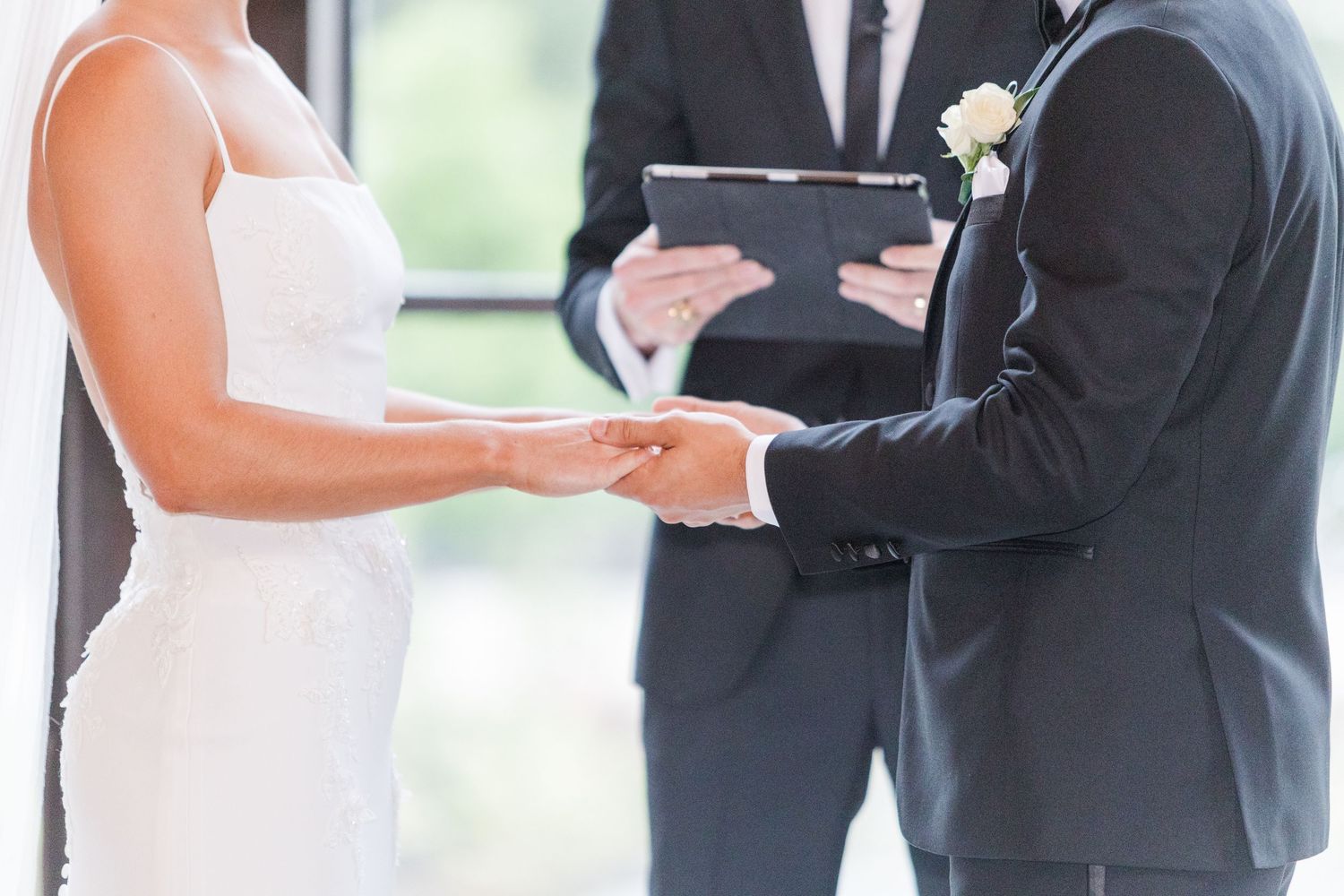 A wedding couple exchanging rings during their ceremony in front of a floral arrangement.