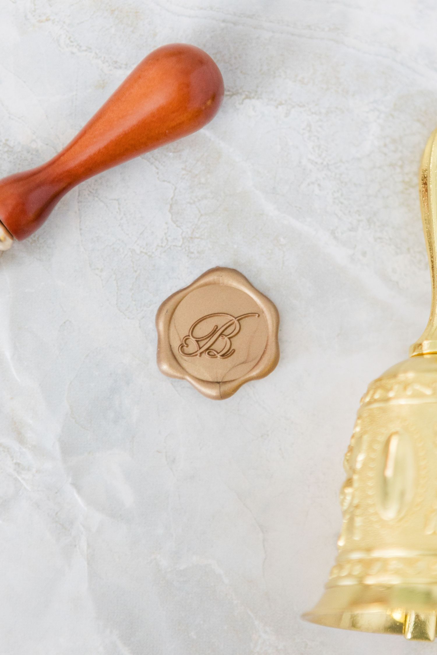 Wooden wax seal stamp and gold wax seal impressions on marble background.
