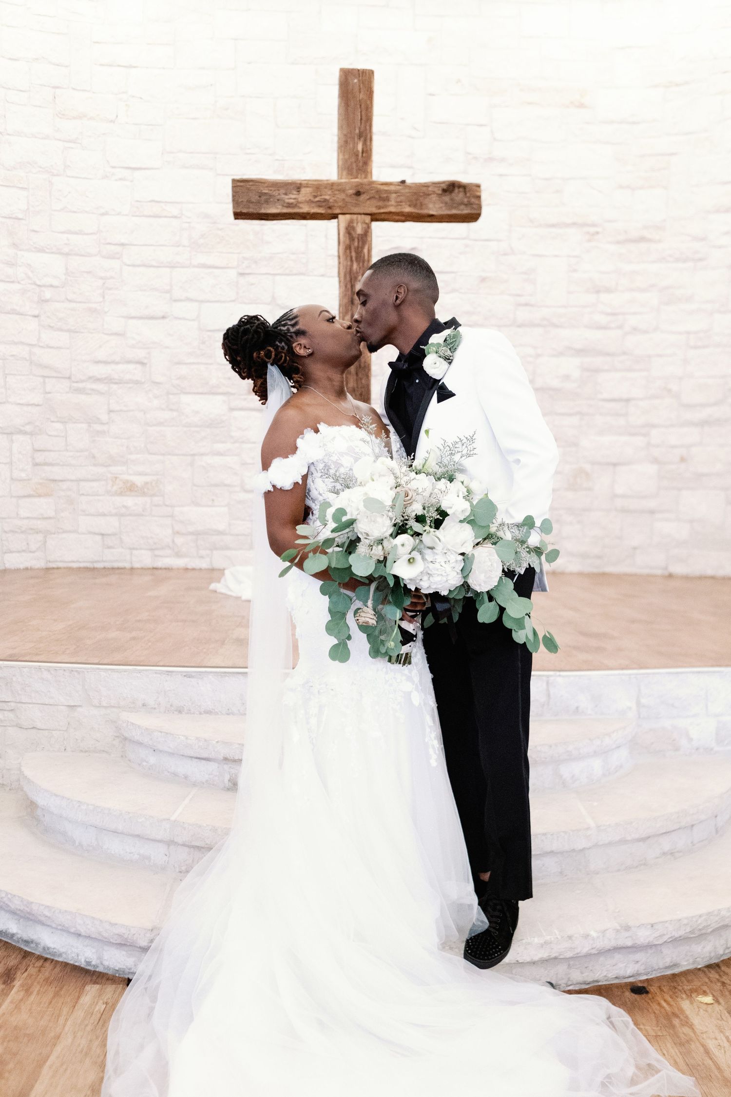 A romantic wedding ceremony moment with a white wooden cross and beautiful floral bouquet in a bright church setting.