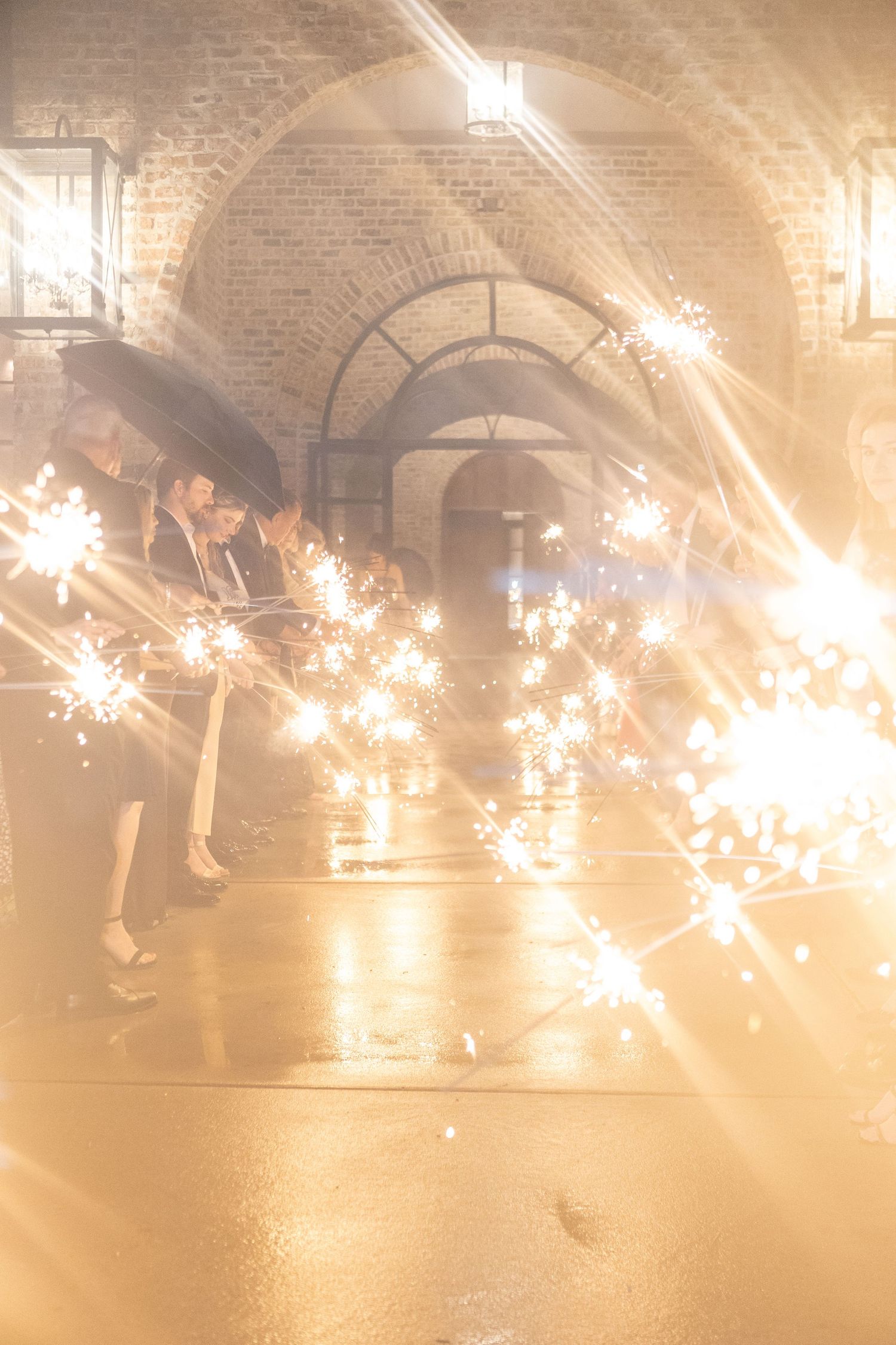 Sparklers create magical light trails against brick archways during a wedding celebration.