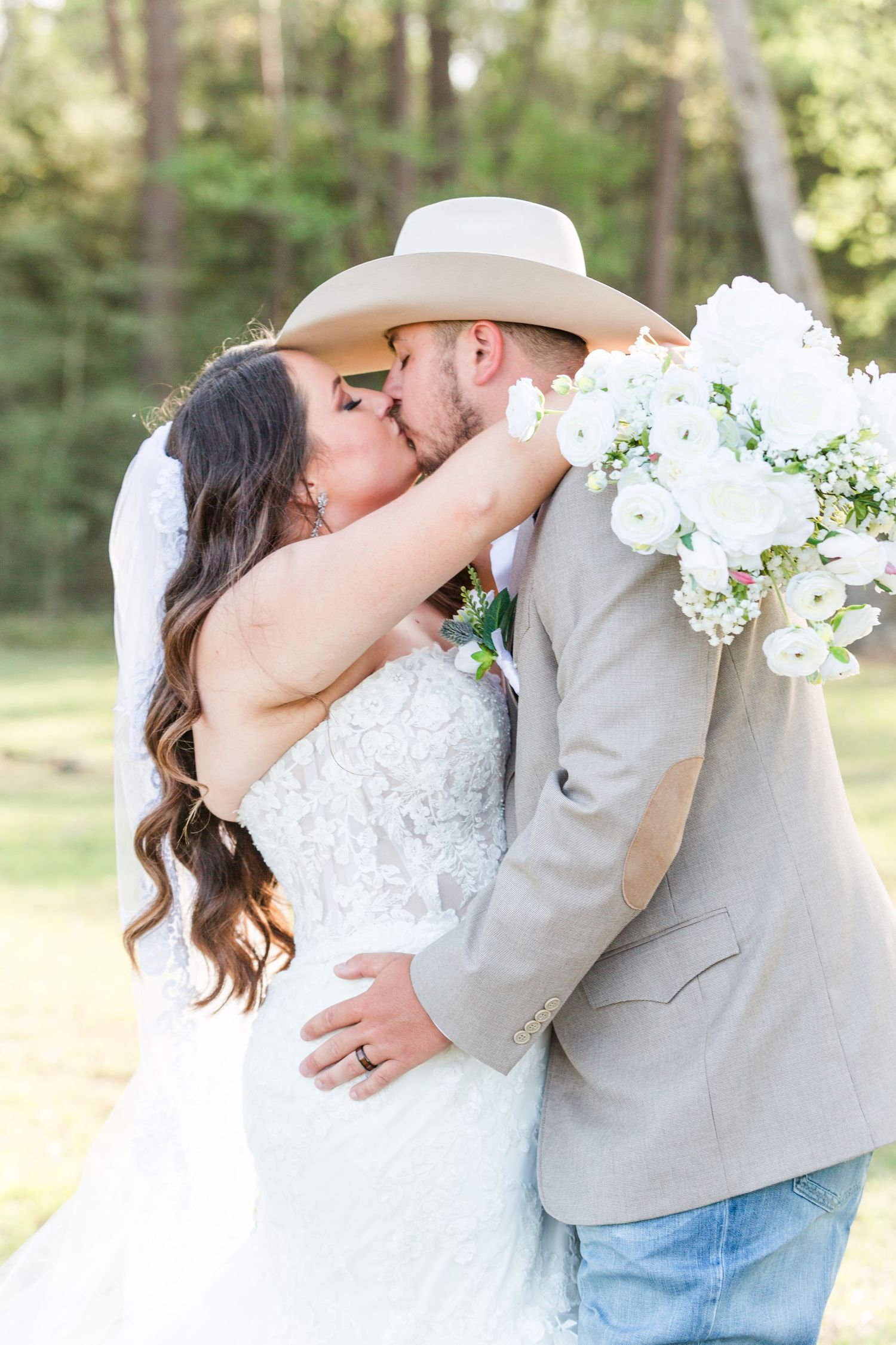 Romantic wedding couple sharing a kiss while holding white floral bouquet.
