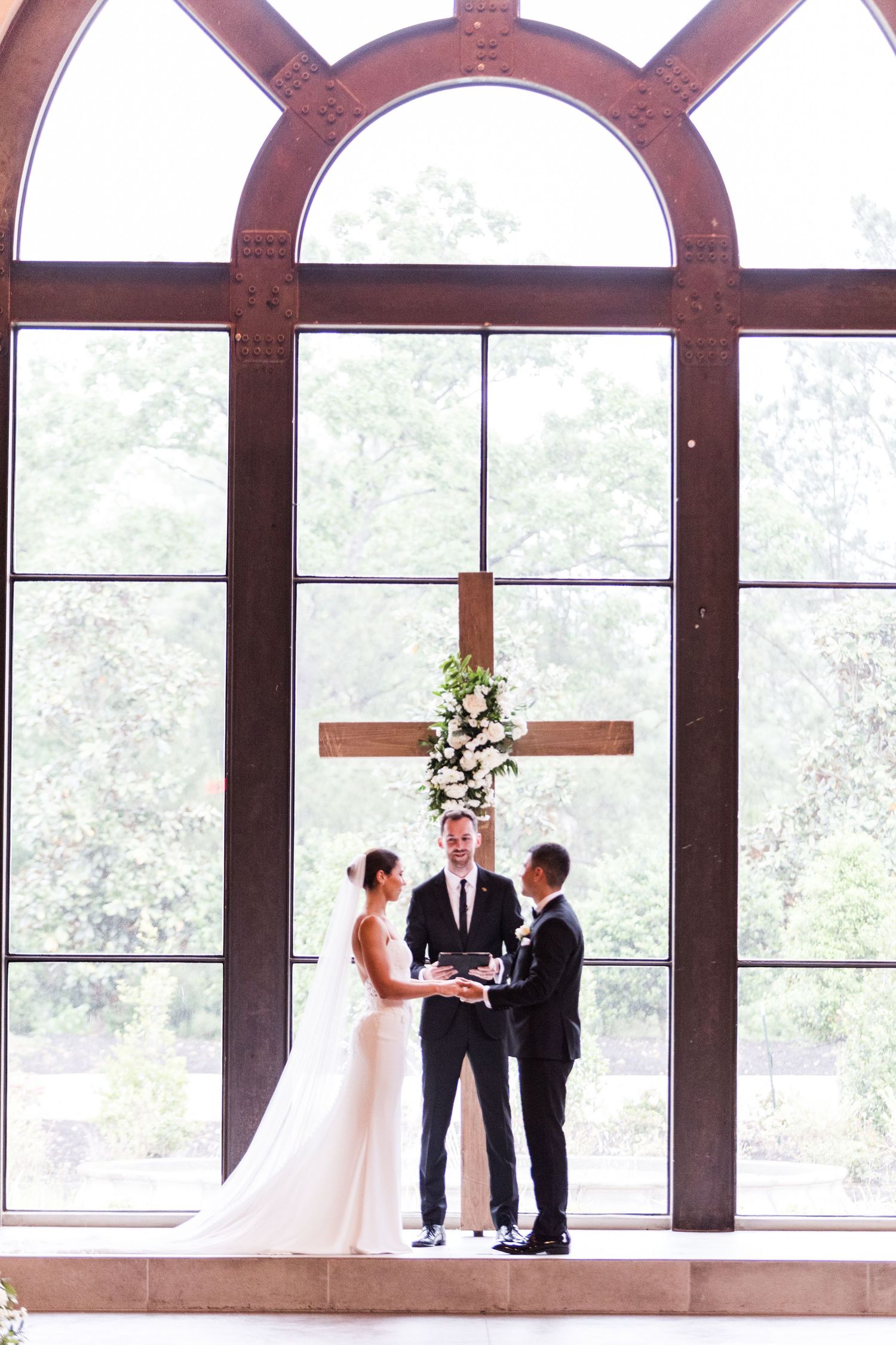 Light-filled ceremony space features arched windows and wooden beams during wedding vows.