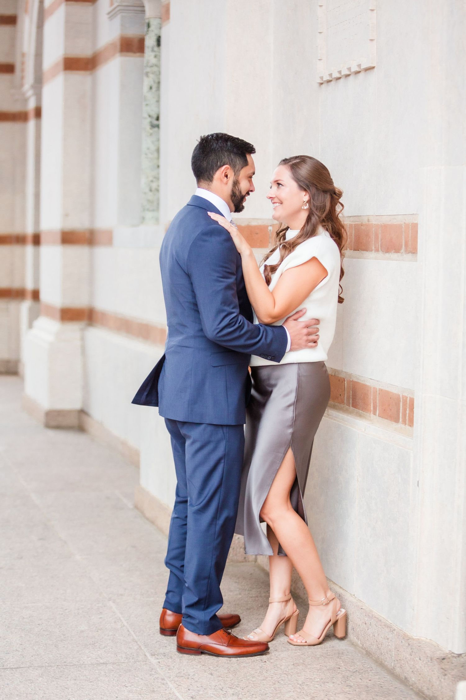 Stylish couple in navy and white share tender moment along ornate building exterior.