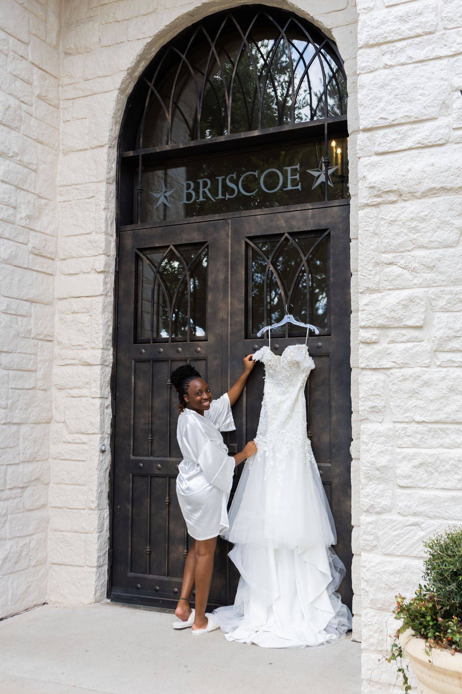 White wedding dress being carried through ornate stone archway entrance.