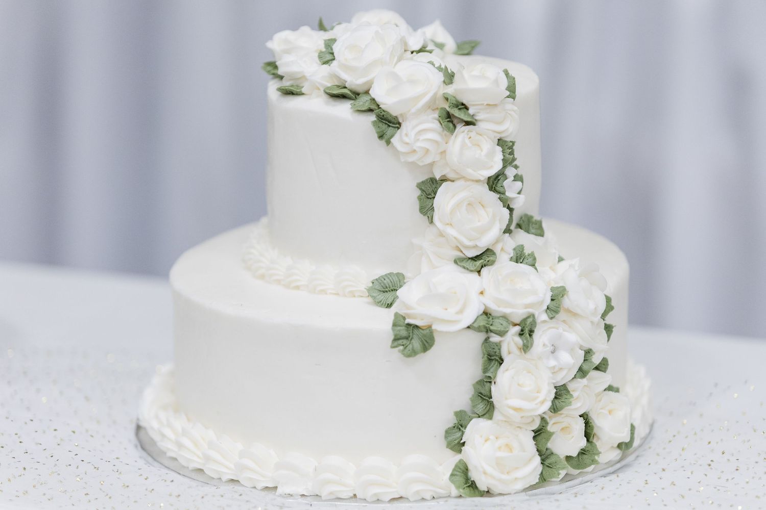 Classic white wedding cake decorated with cascading white roses and delicate greenery against a light backdrop.