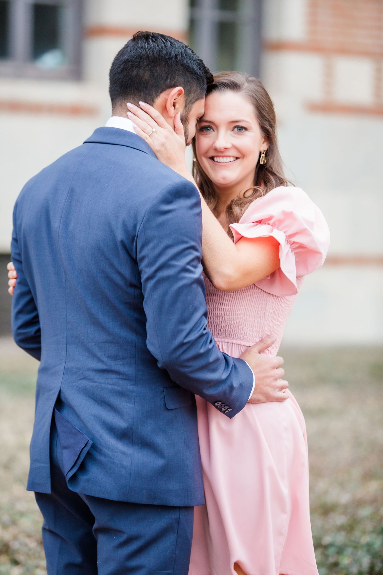Sweet couple embraces in front of a historic brick building with pink and navy outfits.