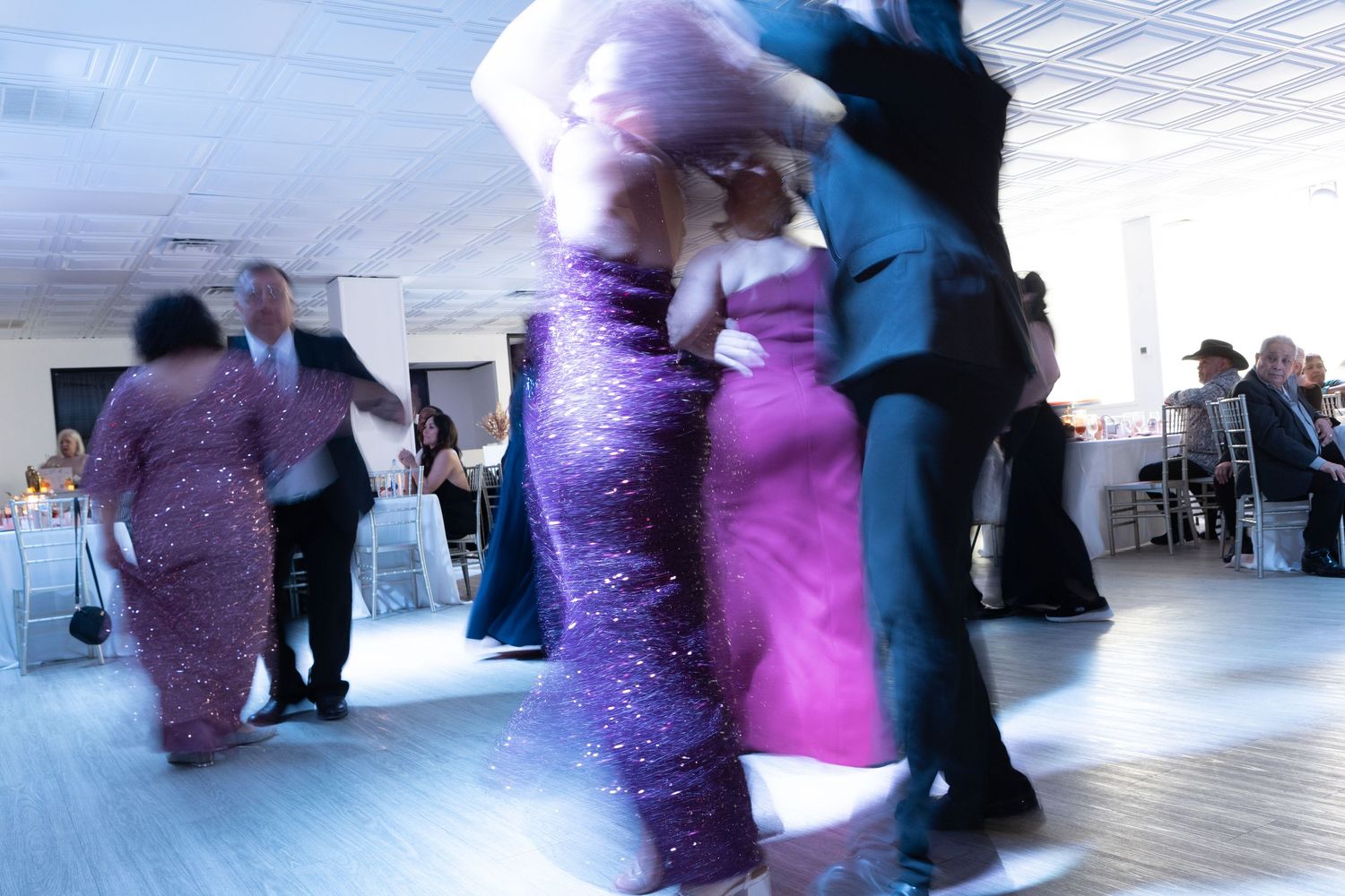 Motion-blurred dancers moving on a dance floor at a reception with colorful formal attire.