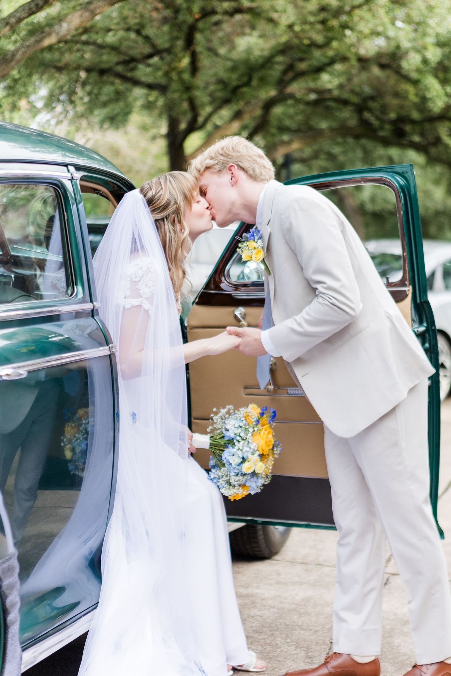 Couple in wedding attire interacting near vintage car door.