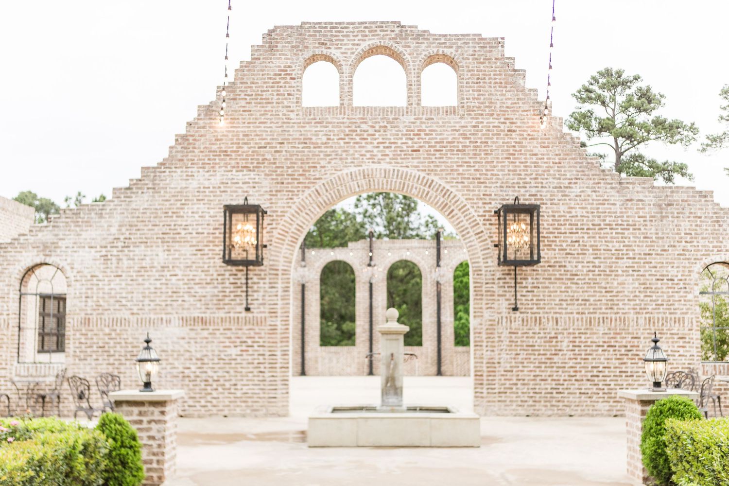 Brick archway entrance to an outdoor wedding venue with hanging lanterns.