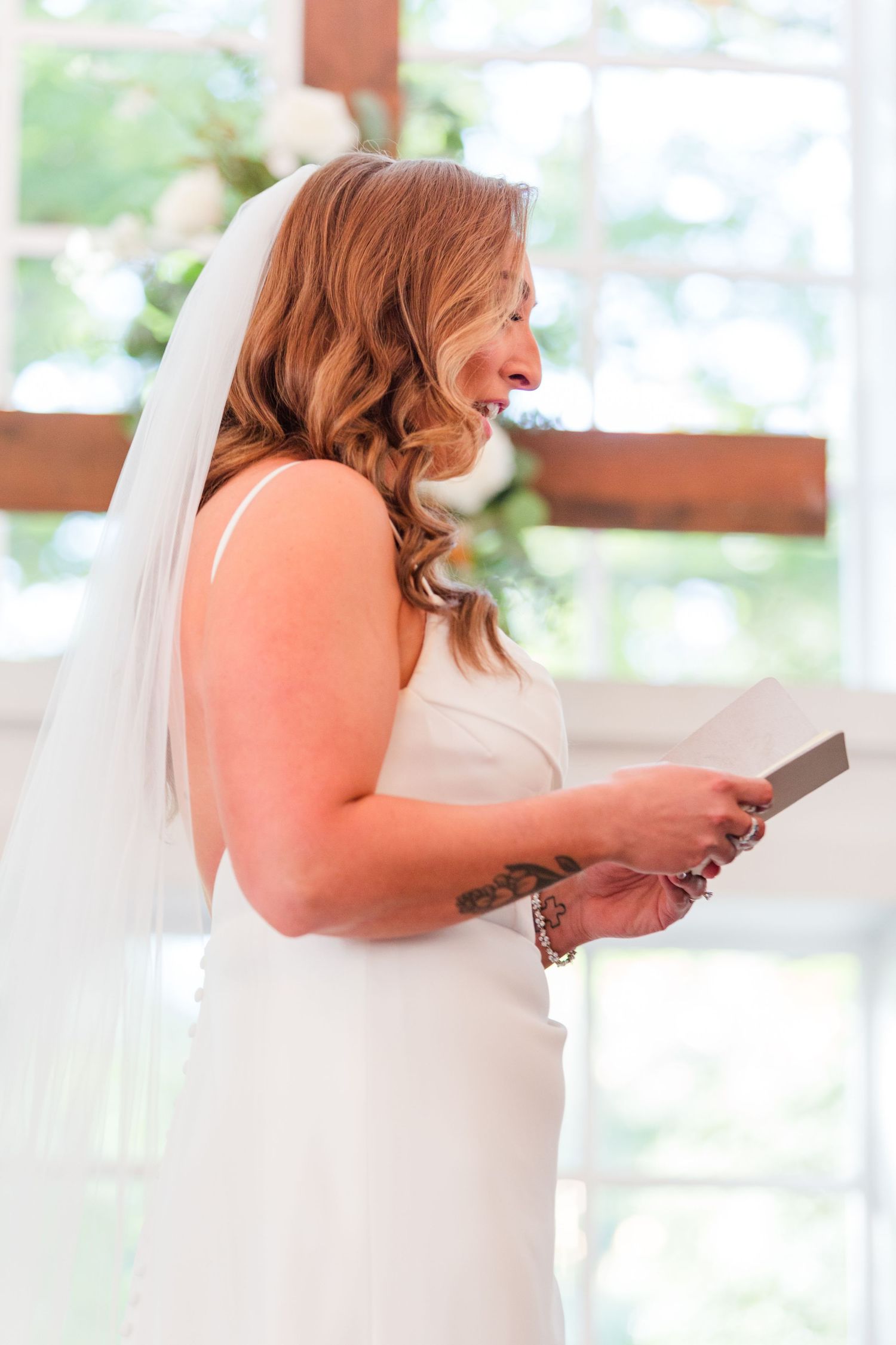 Side view of bride in white dress reading from booklet during ceremony.