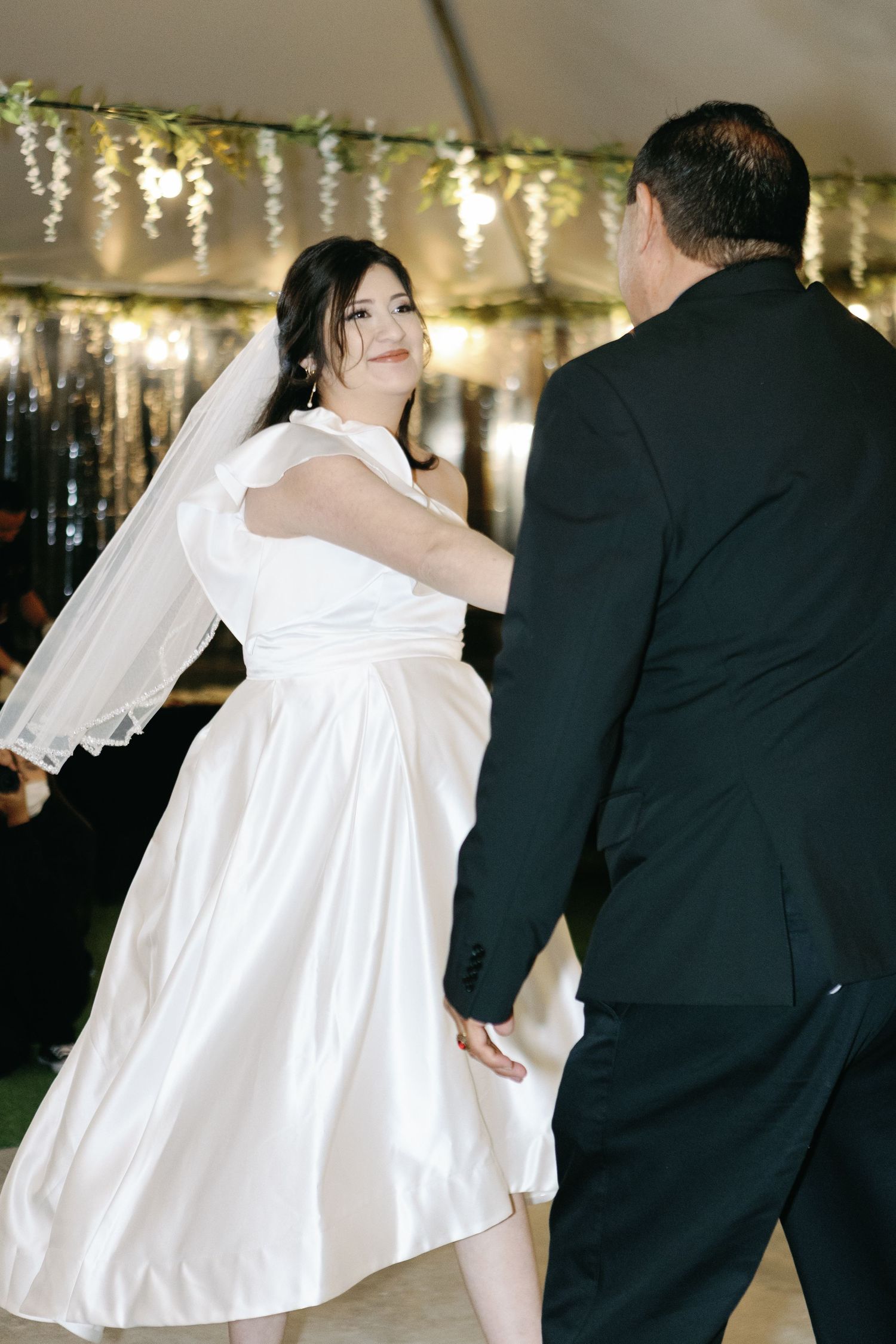 Wedding couple dancing under twinkling lights at an evening reception.