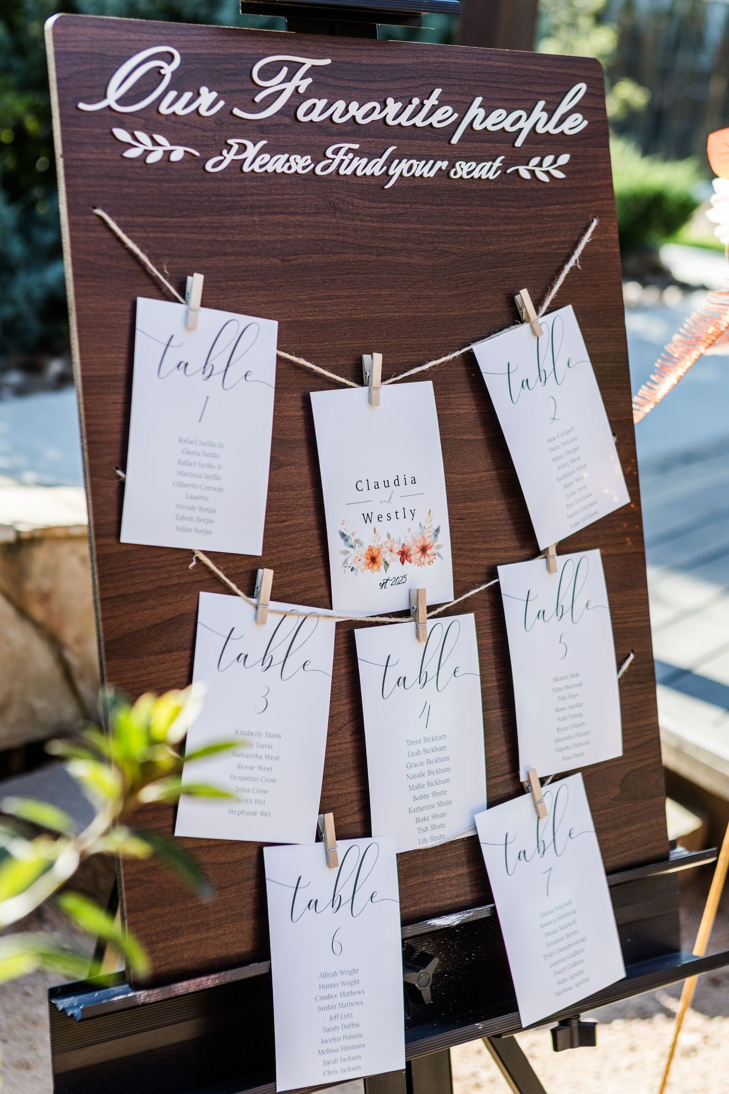 Rustic wooden wedding seating chart display with white cards hanging from twine showing table assignments.