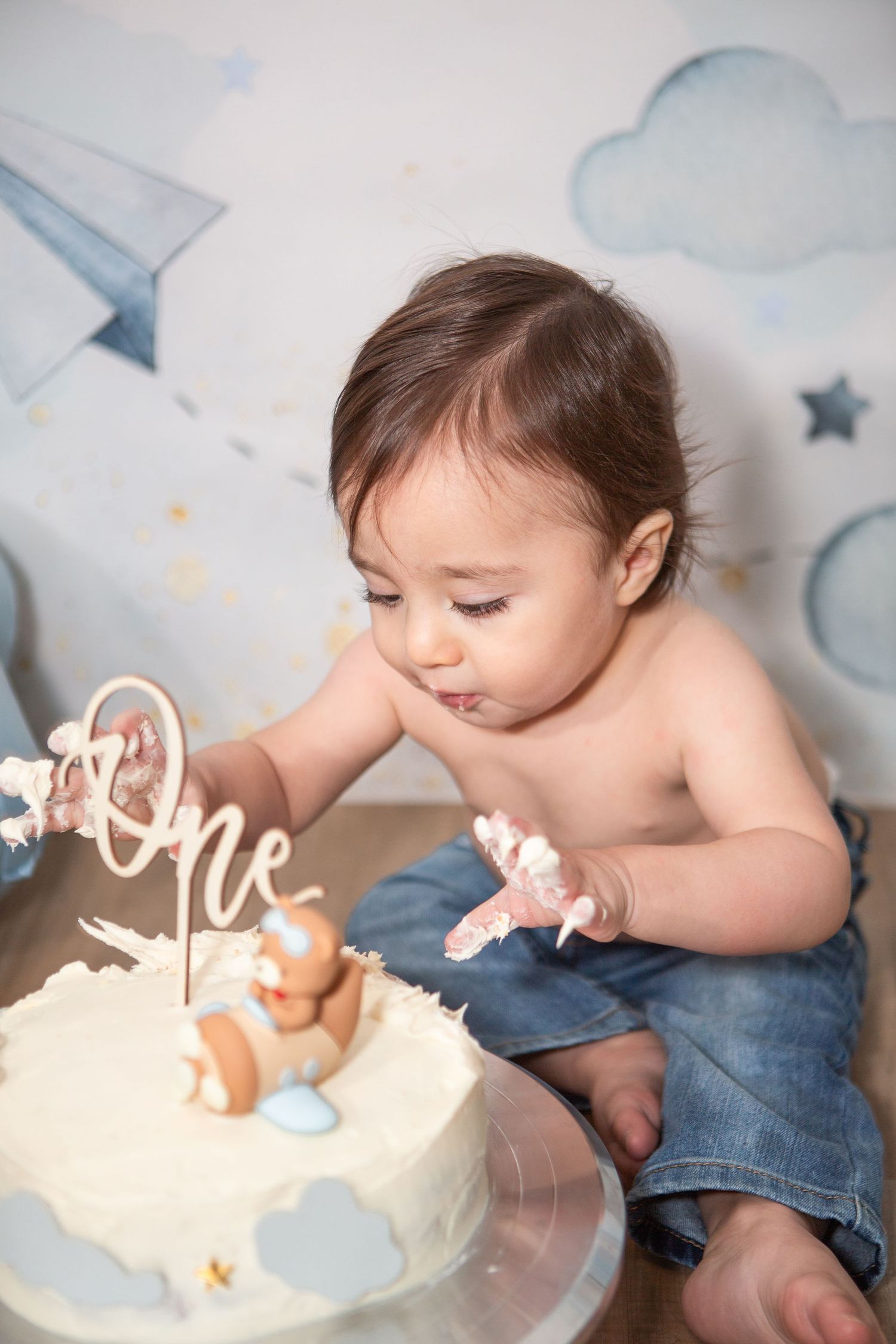 Baby in jeans enjoying their first birthday cake smash session.