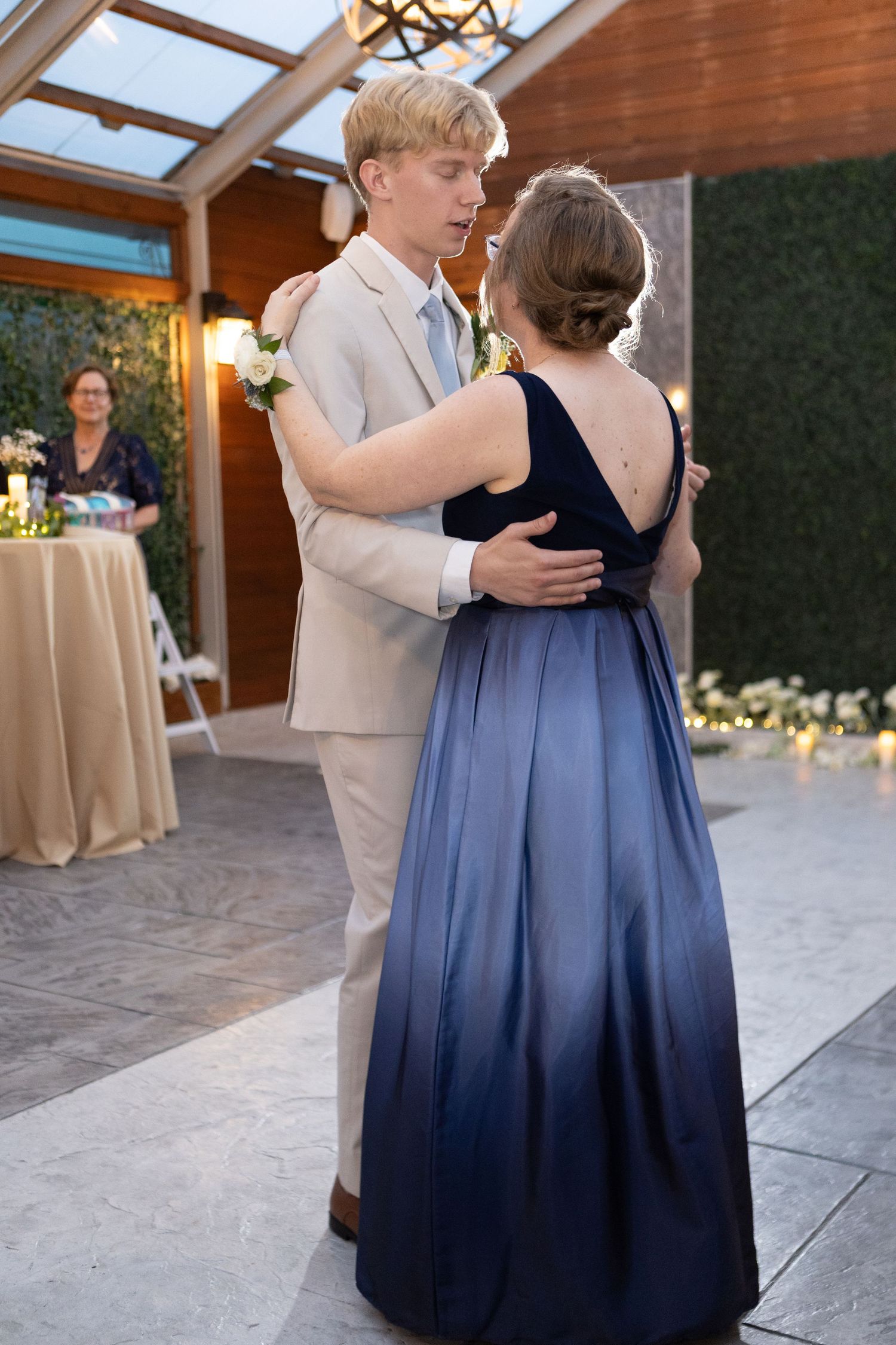 Guests dancing at a wedding reception in navy blue attire beneath rustic wooden architecture.