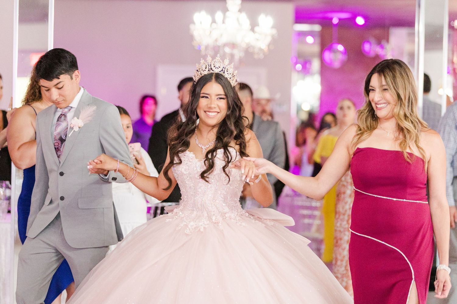 Dancing celebration in an elegant venue with chandeliers and purple accent lighting.