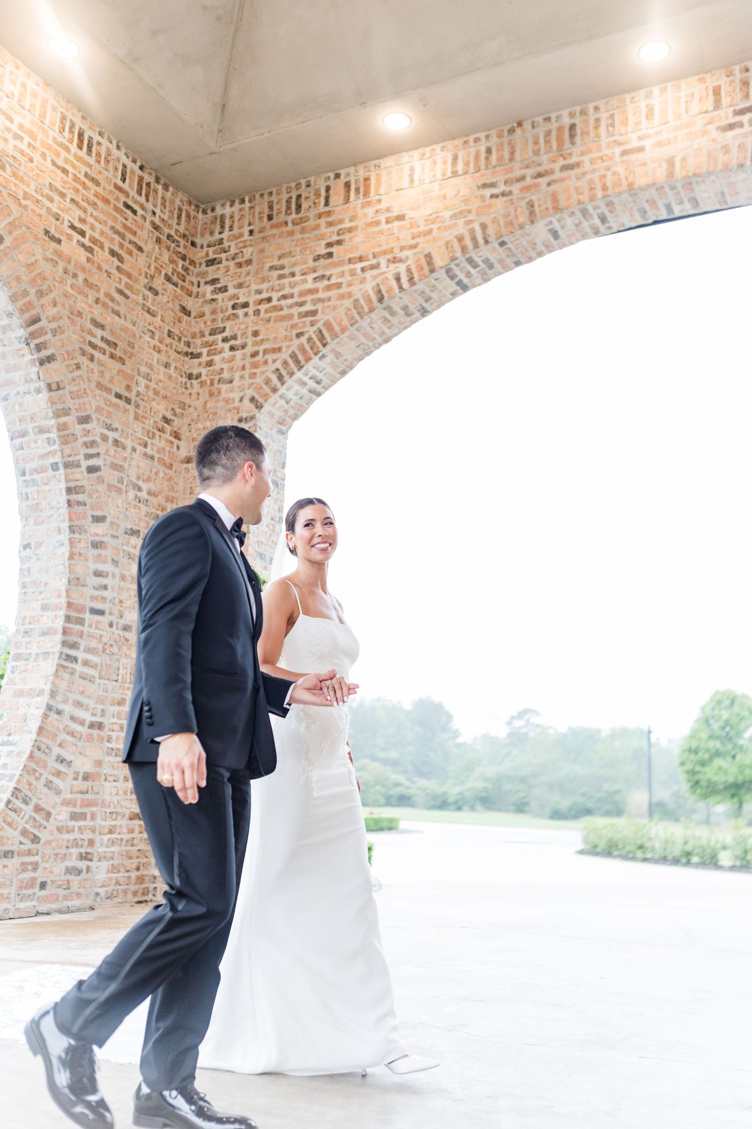 Candid moments of a couple's first look captured under a brick archway.