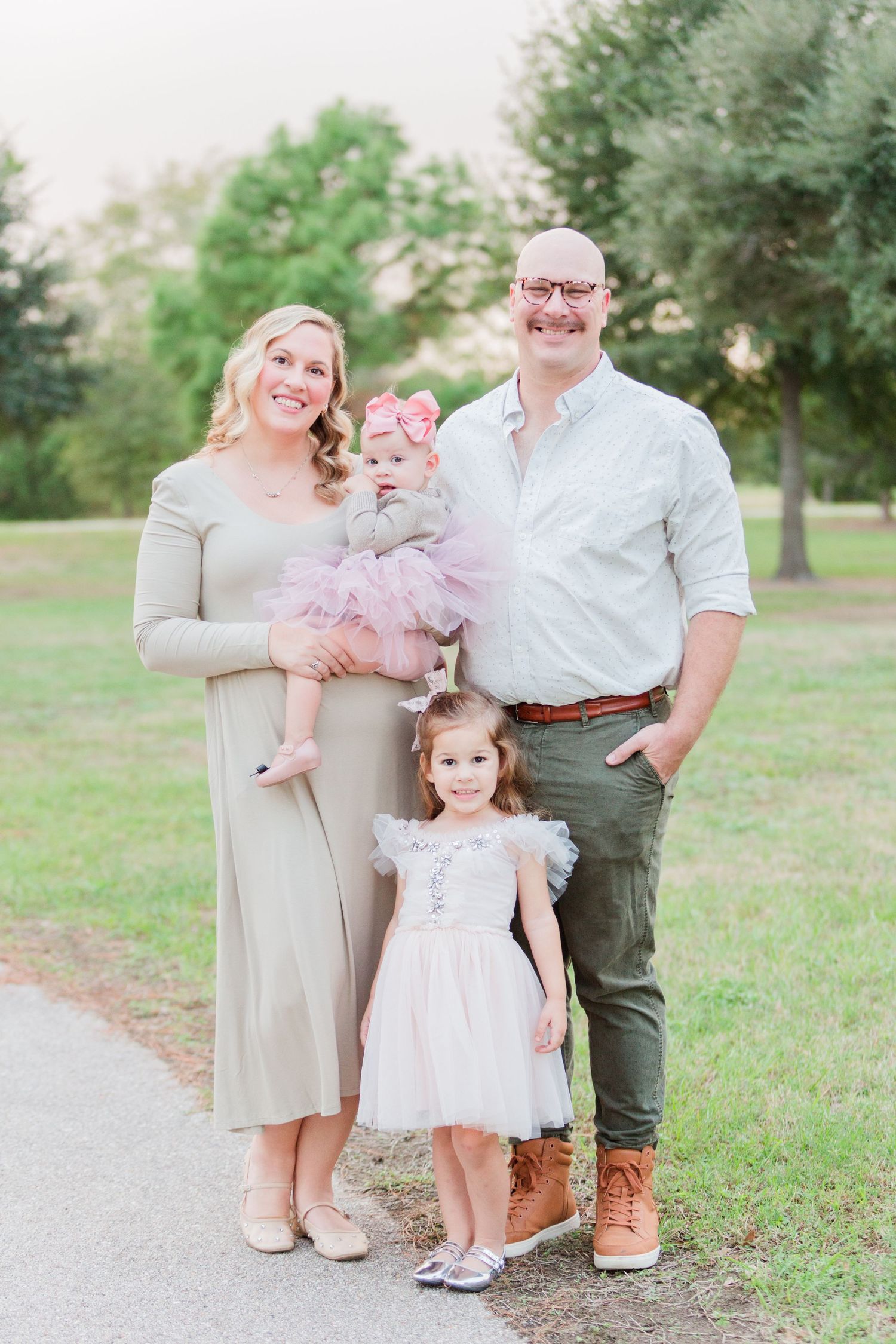 Family group in neutral tones poses together on outdoor path surrounded by greenery.