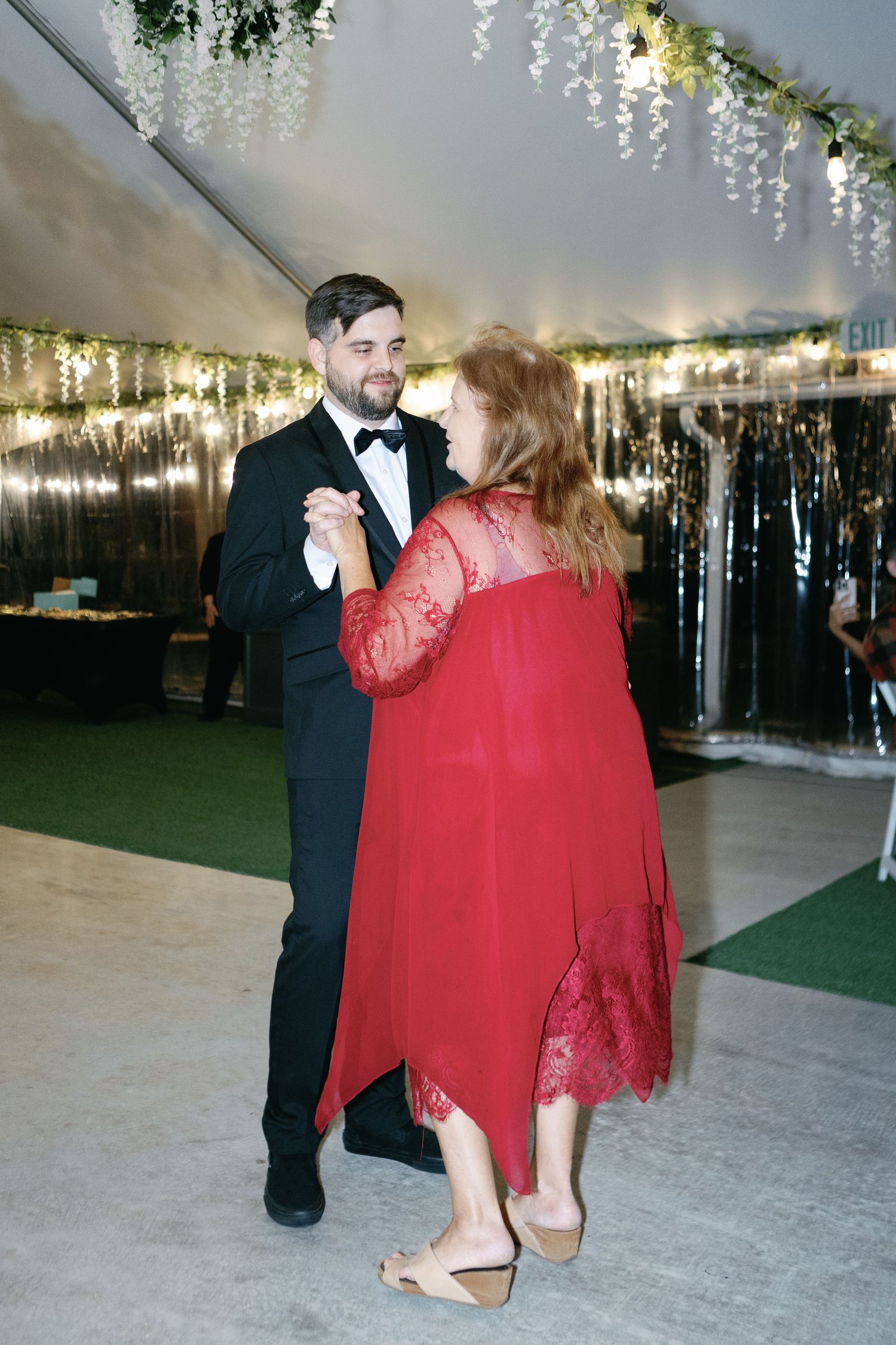 Dancing under twinkling lights at wedding reception with red dress highlight.