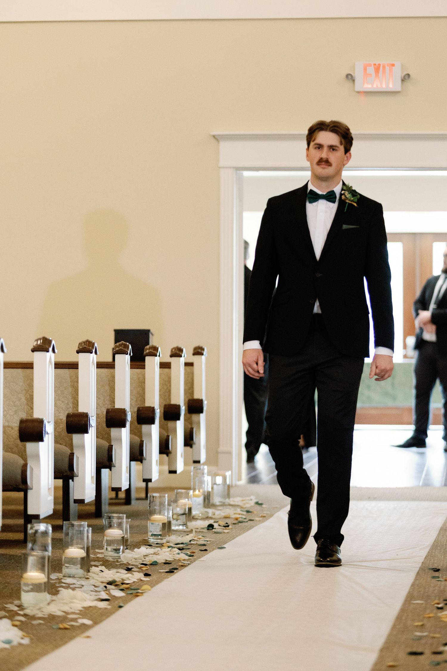 Person in formal black suit walks down church aisle with decorative white pillar details.