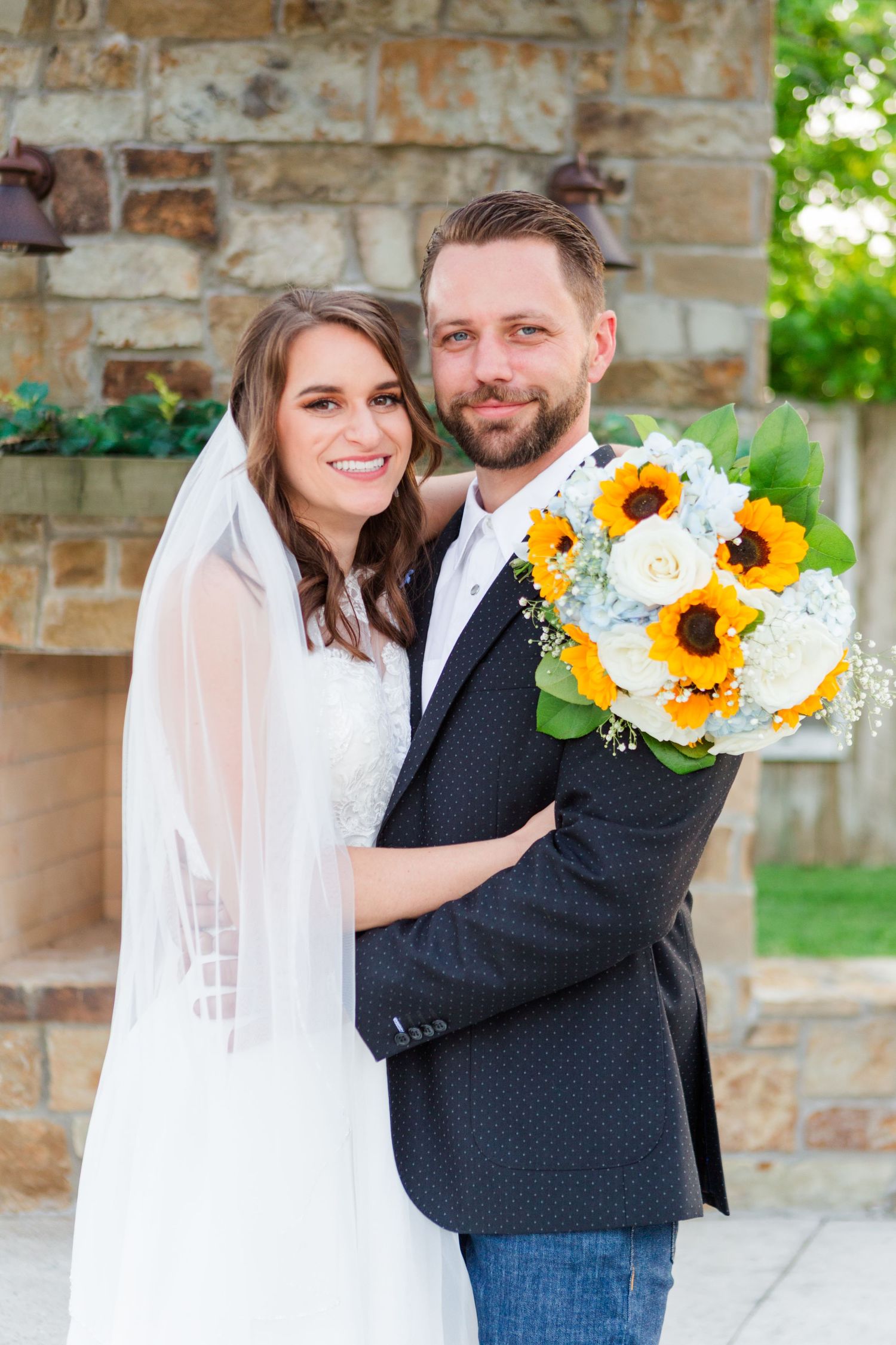 Joyful wedding portraits with sunflower bouquet against stone architecture.