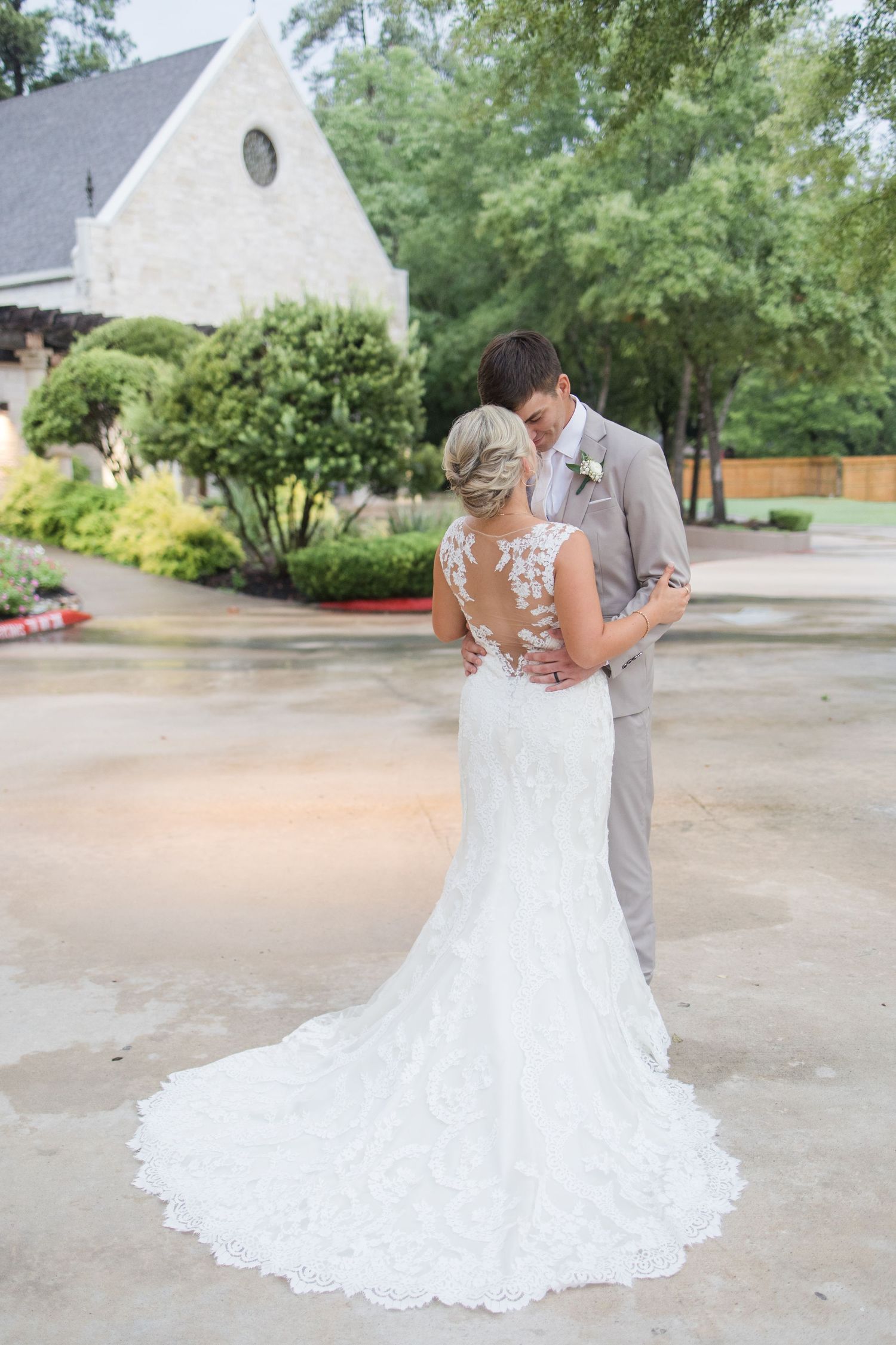 Wedding dress with intricate lace train captured from behind against outdoor chapel backdrop.