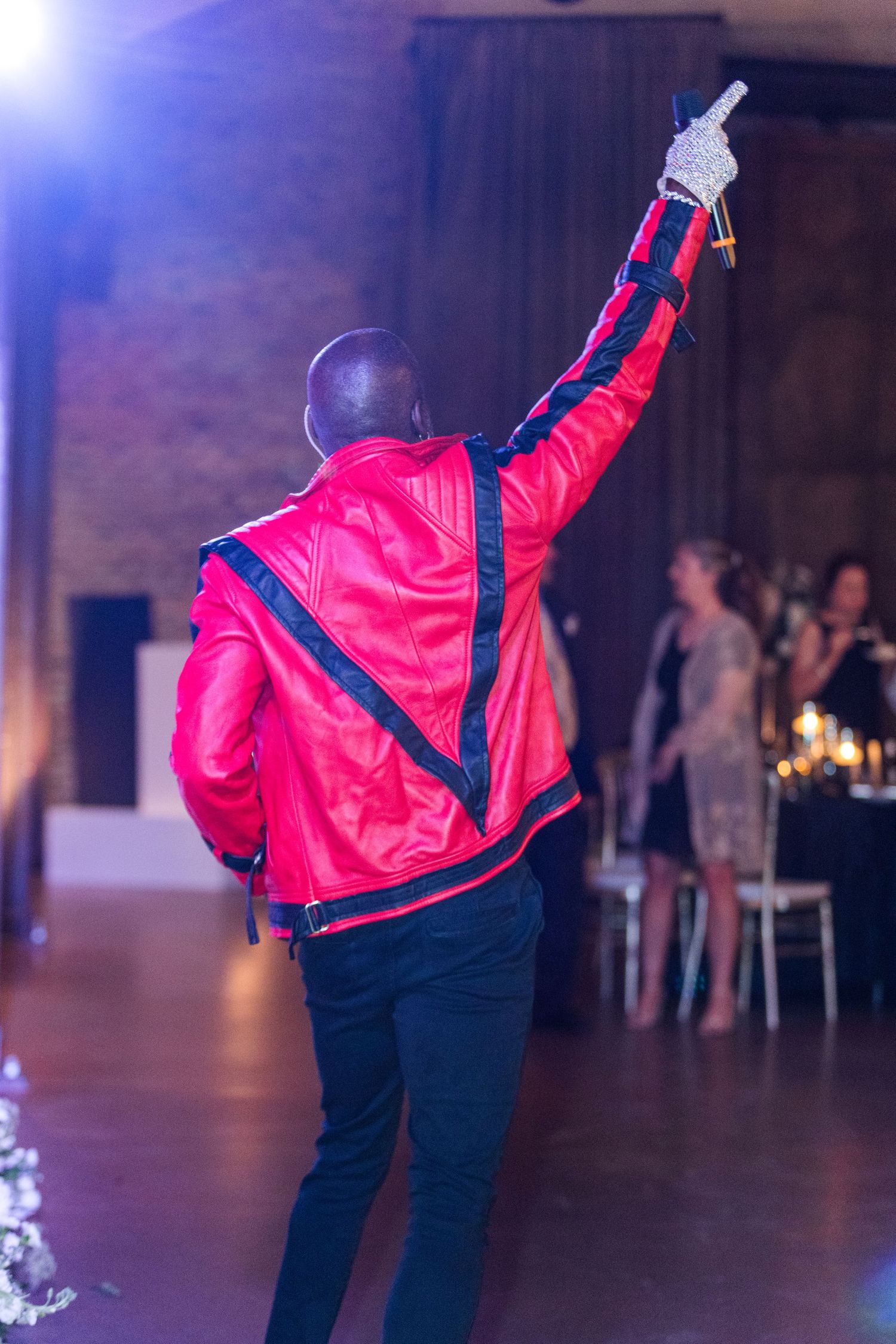 Dancer in red jacket performs against dark backdrop during indoor event.