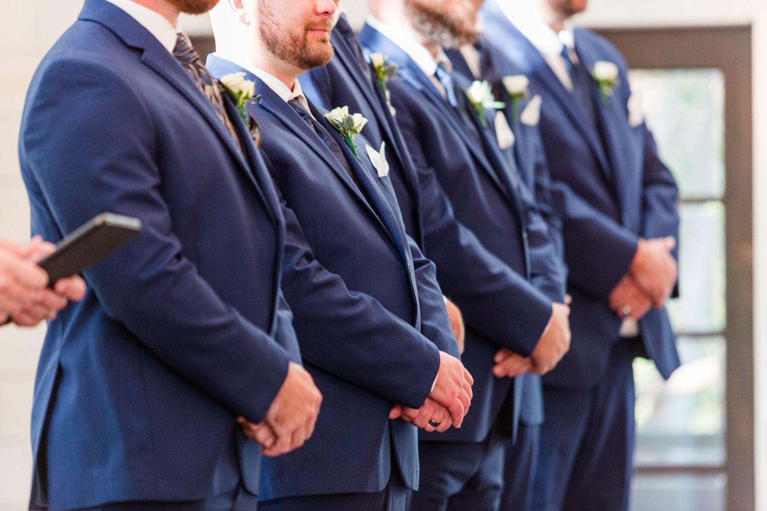 Groomsmen in navy blue suits standing in line at a wedding ceremony.