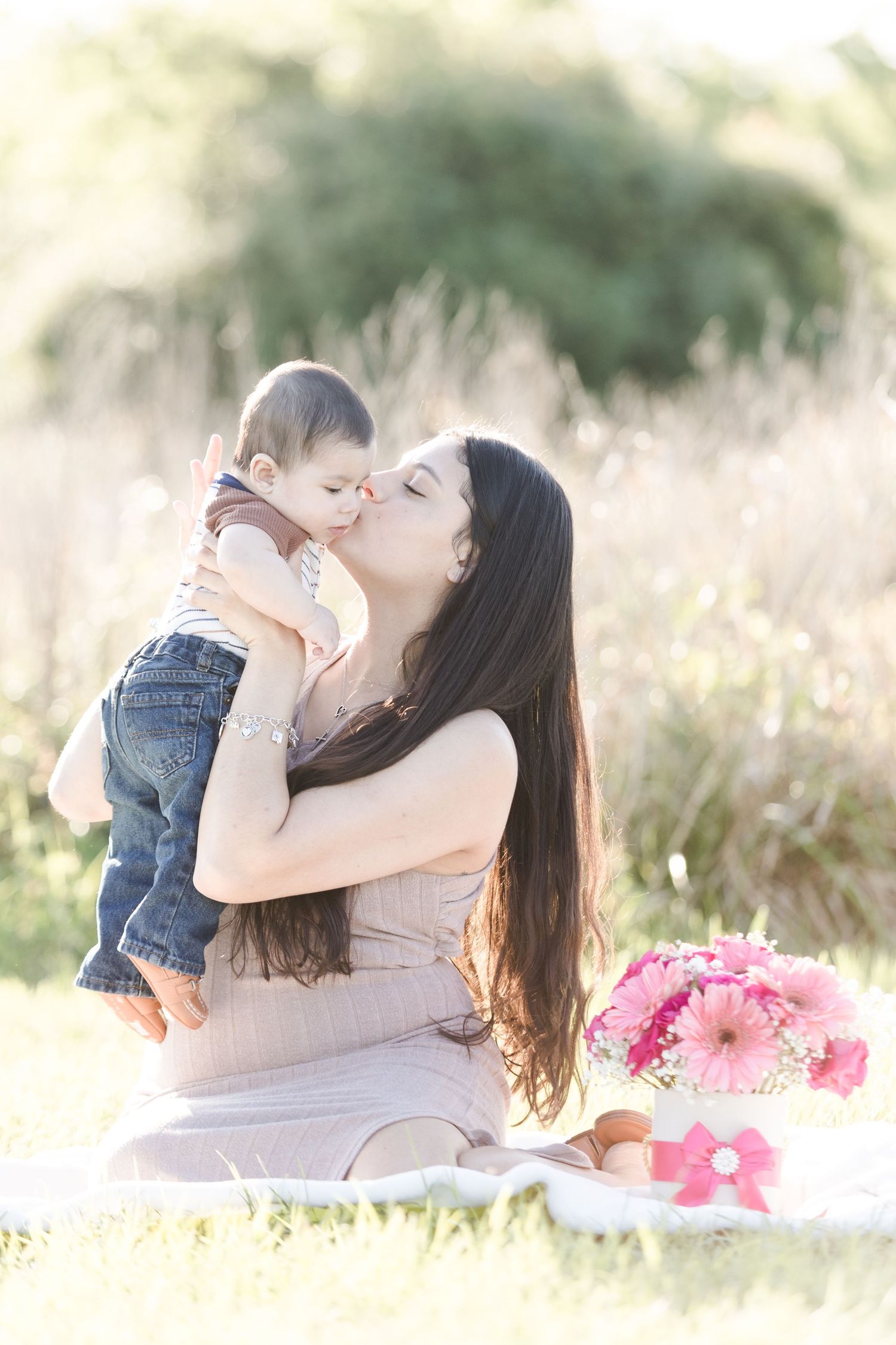 Mother and child sharing tender moments in a sunlit field with pink flowers.