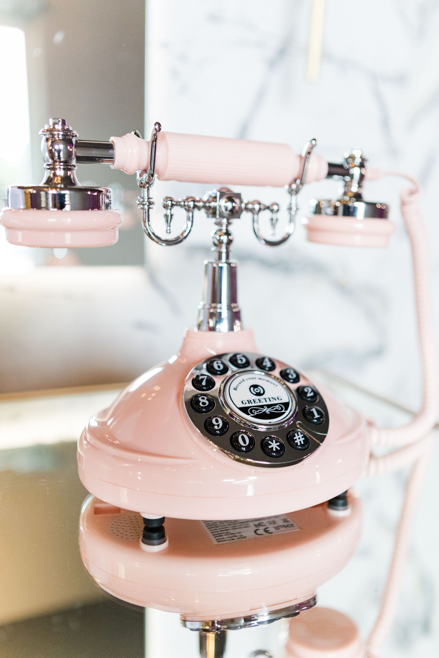 Vintage pink rotary telephone with silver accents against a marble background.