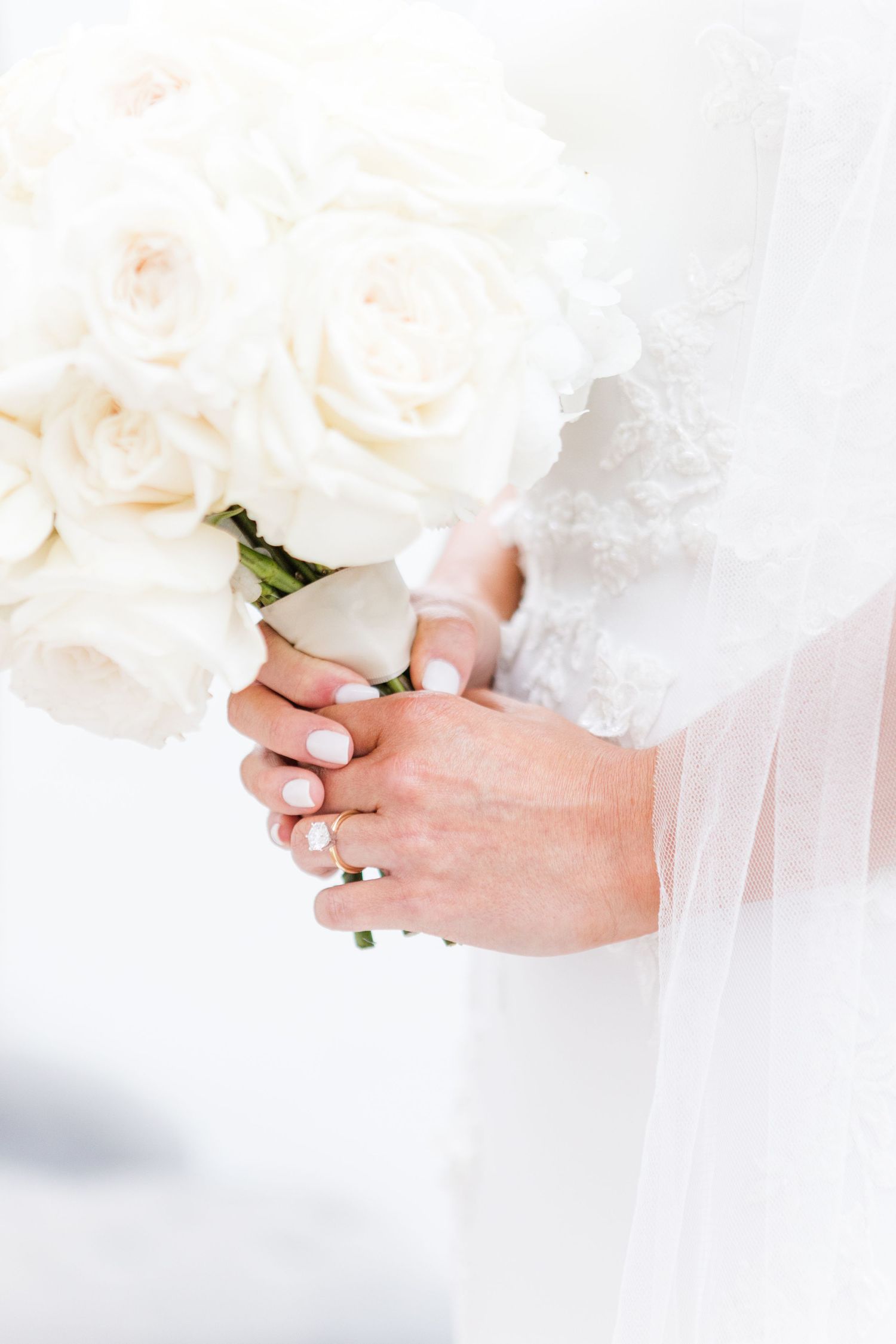 Delicate white rose bouquet held by bride in soft natural light.