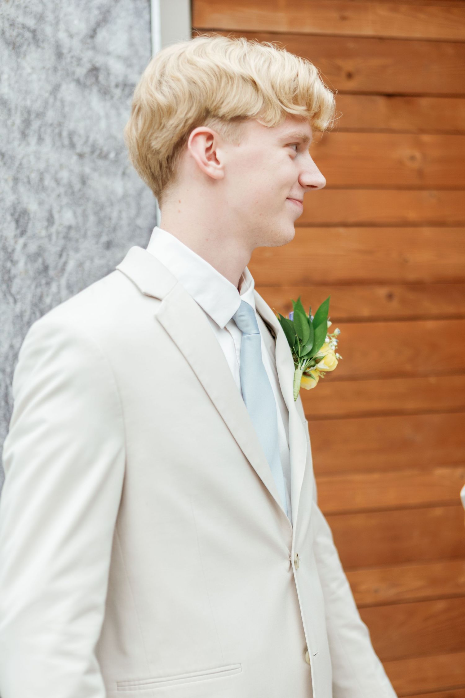 Close-up profile shot of person in light colored suit against wooden wall background.