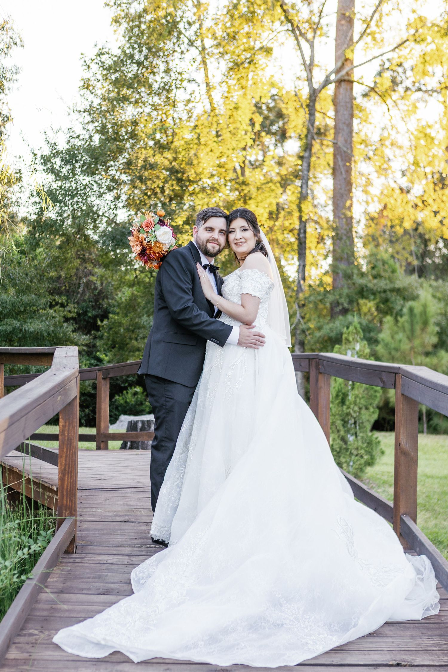 Romantic wedding photos on wooden boardwalk surrounded by autumn trees.