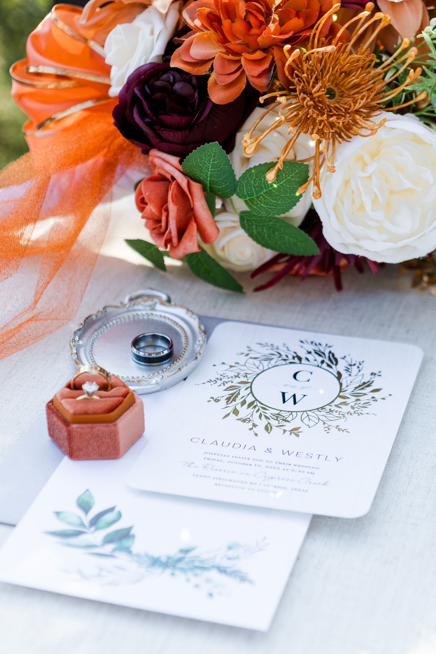 Wedding invitation suite with orange and burgundy flowers and elegant calligraphy design on white paper.