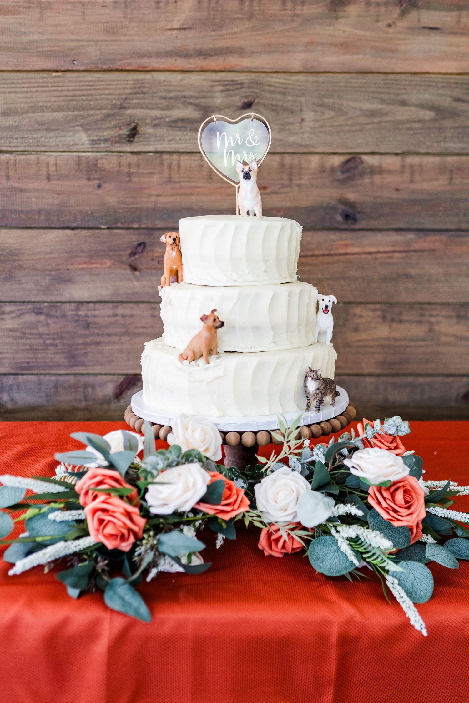 Three-tiered white wedding cake decorated with small animal figurines and coral roses.