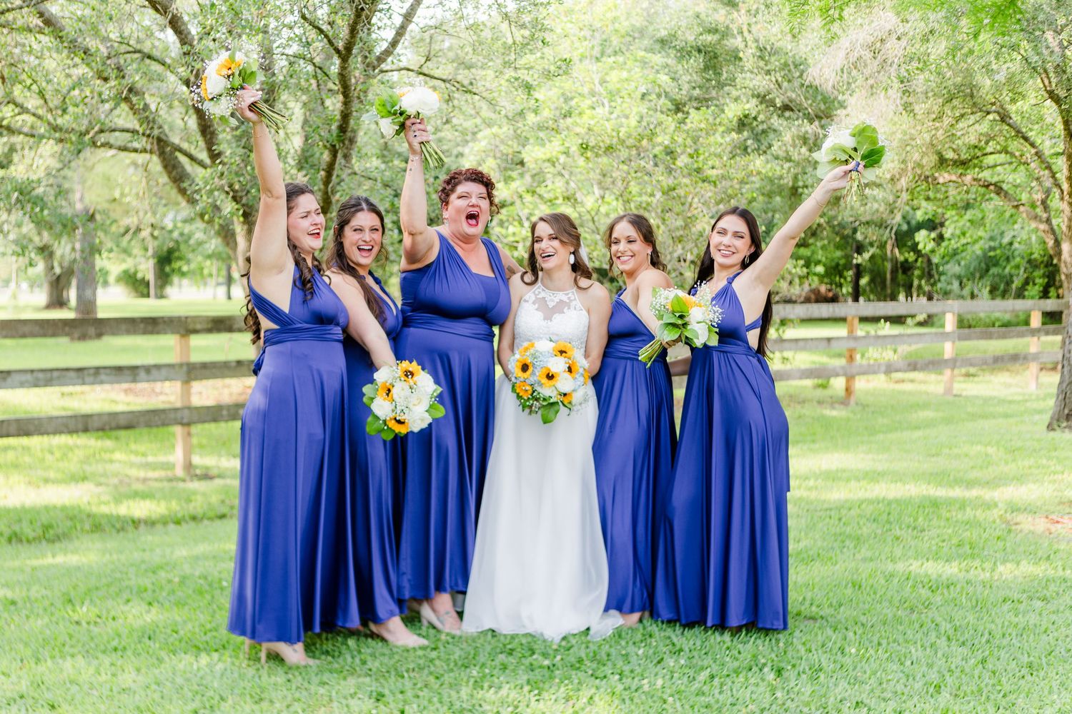 Bridesmaids in royal blue dresses pose with bride on green lawn.