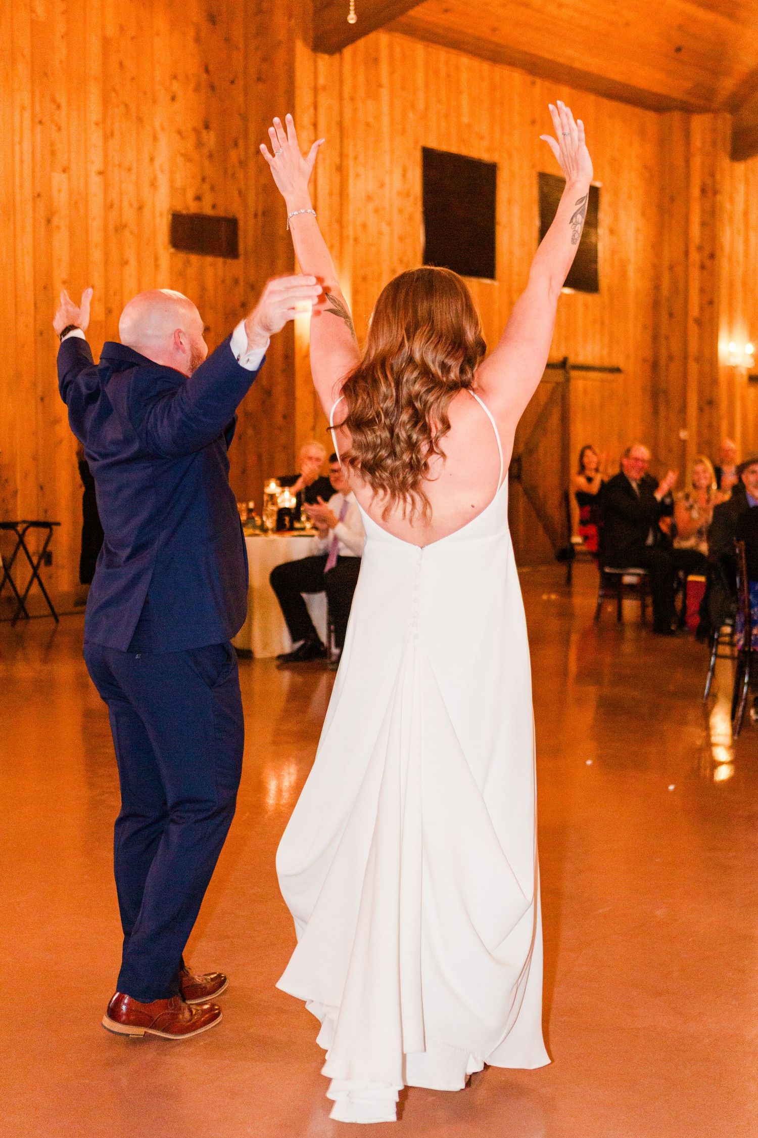 Wedding guests dancing with raised arms in a rustic barn reception venue.
