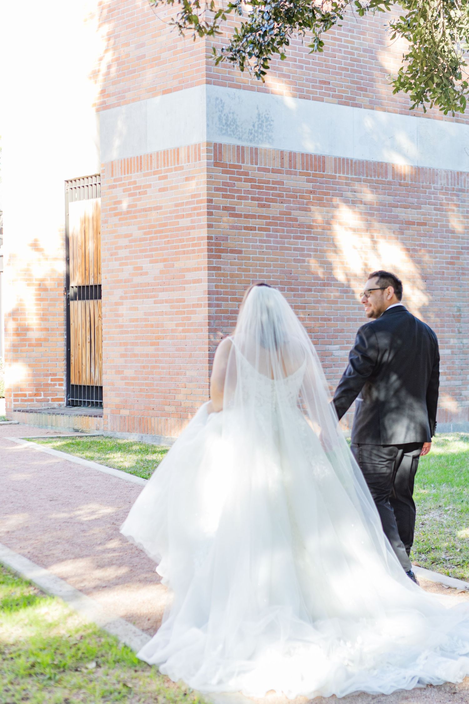 Wedding couple poses against brick walls with flowing white dress creating dramatic movement.